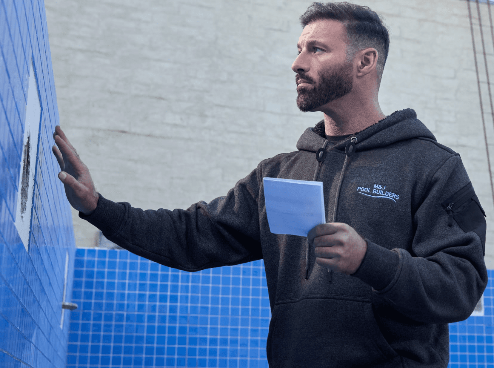 Tradesman standing inside an empty pool holding a tile