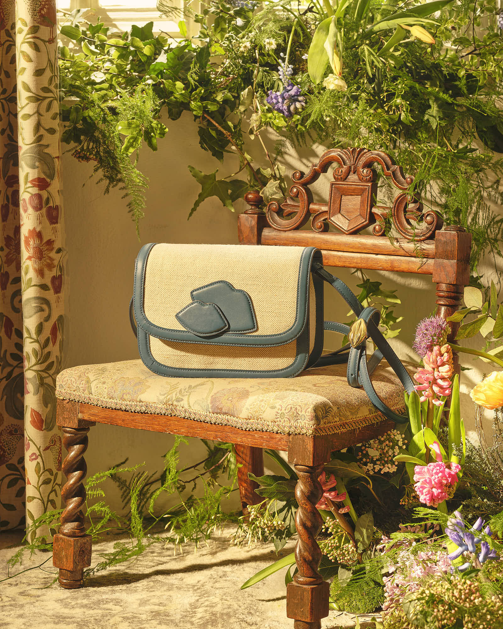 Elegant handbag on ornate vintage chair surrounded by lush greenery and flowers.