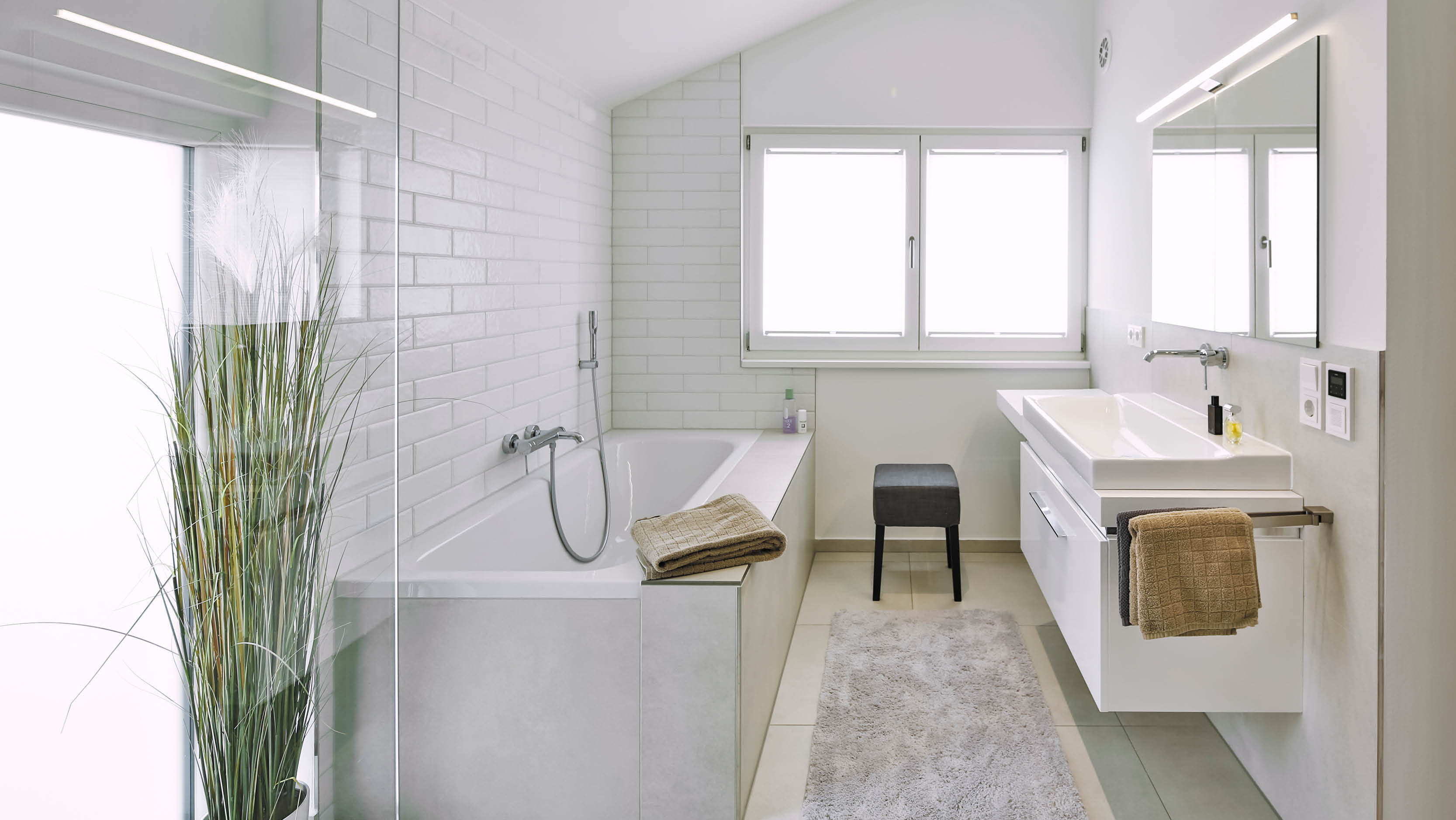 Geräumiges, modernes Badezimmer mit freistehender Badewanne, Waschtisch mit Einbaumöbeln, Spiegel und Fenster.