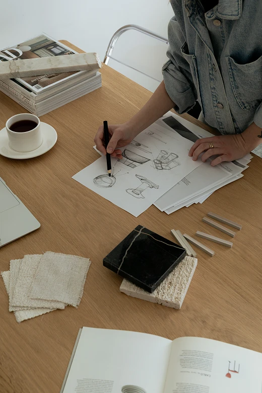 An interior designer's hands arranging a selection of beautiful material samples, including various marble, stone, and wood finishes.