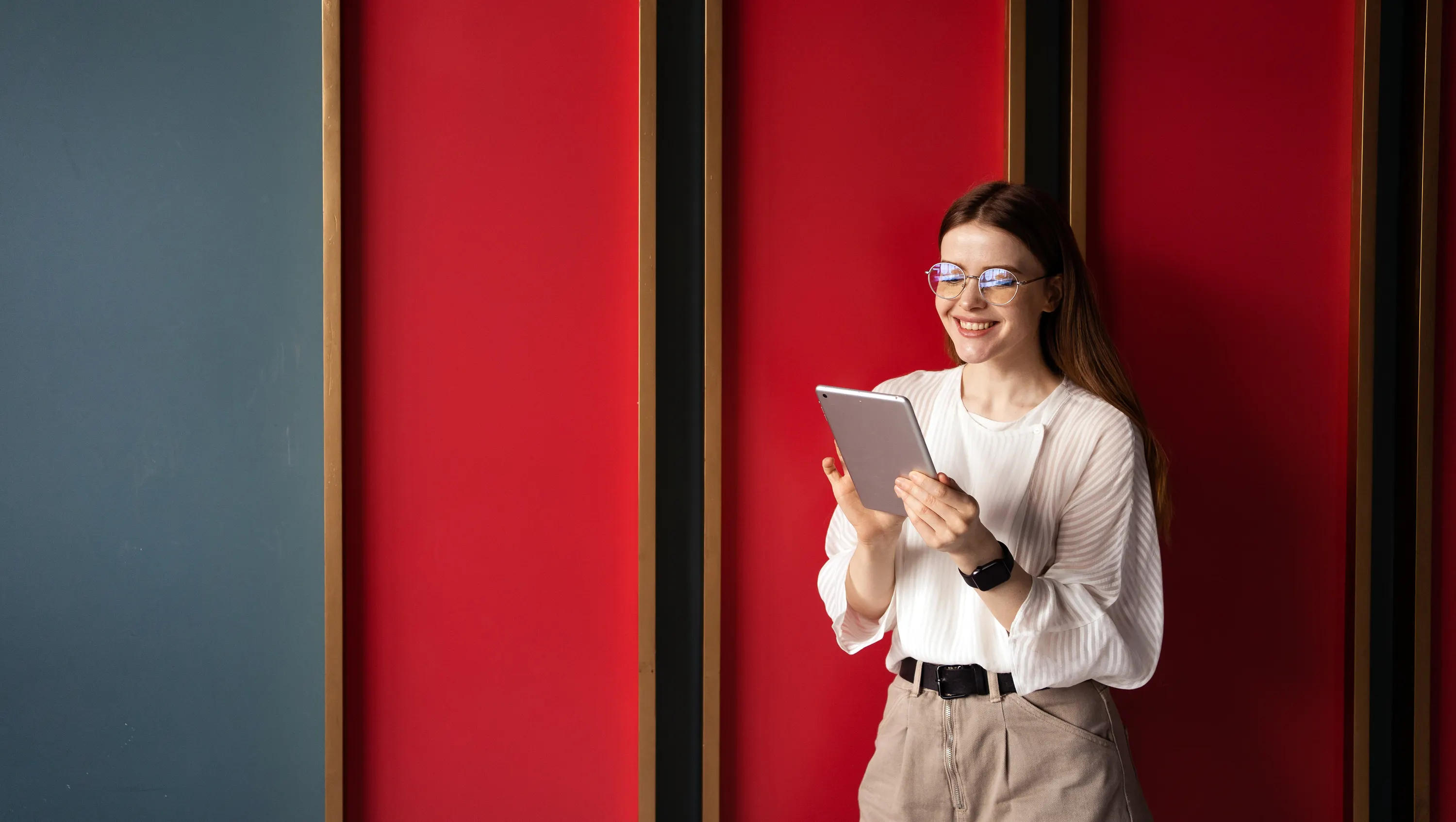 mulher de oculos e com um ipad em frente a fundo vermelho e preto