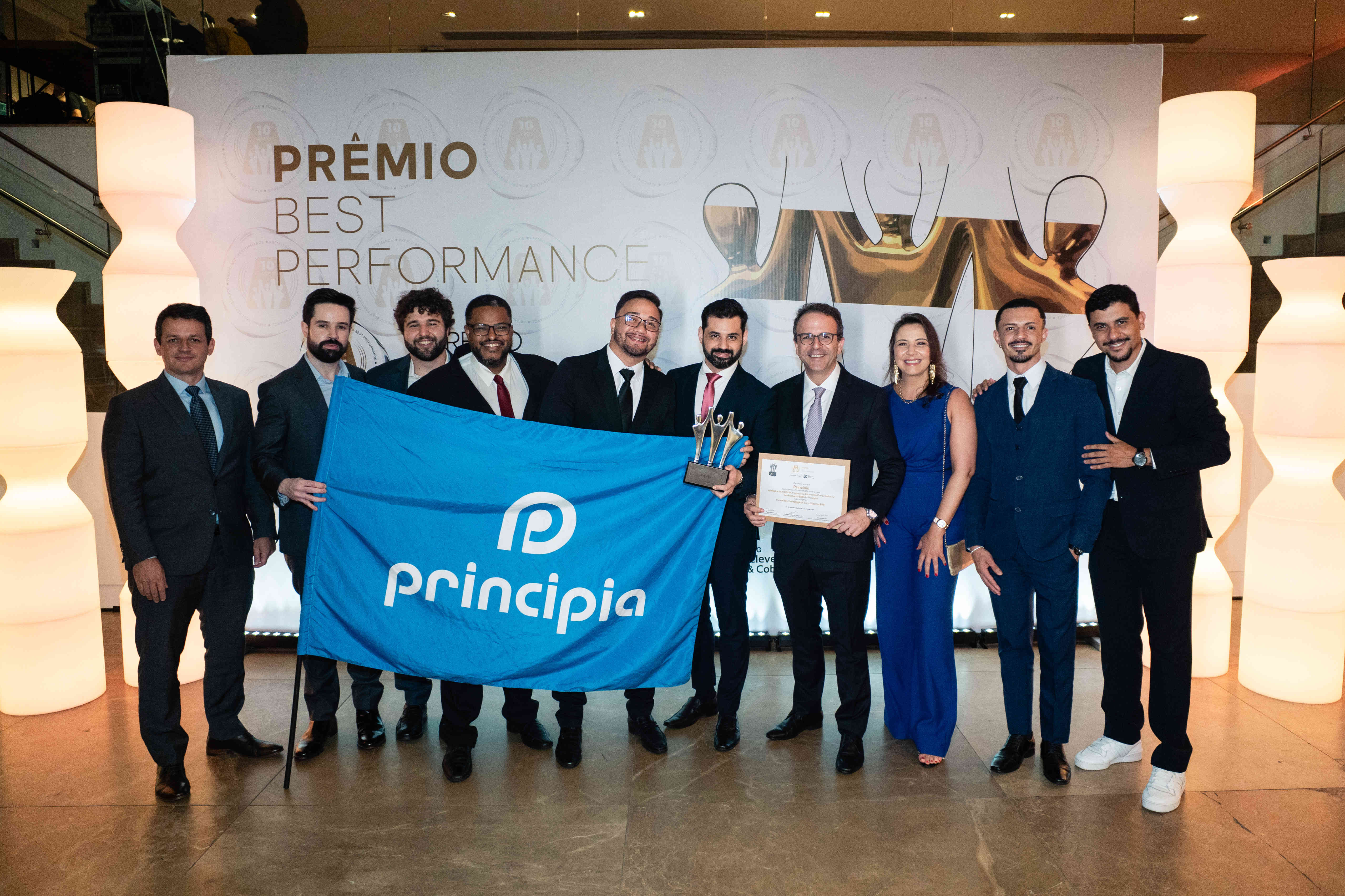 Executivos da Principia posando com troféu prata e certificado no palco do Prêmio Best Performance 2025