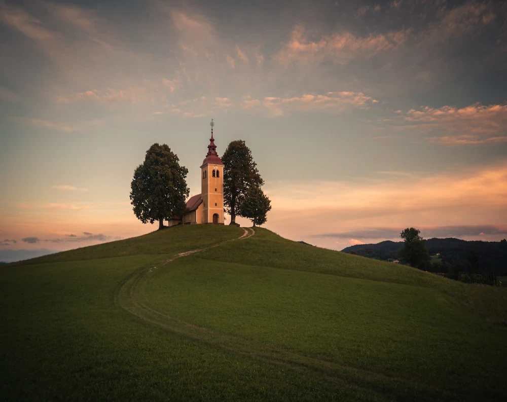 Sveti Tomaž Church at Vrsnik during sunset, with a winding road leading up through the grassy fields.