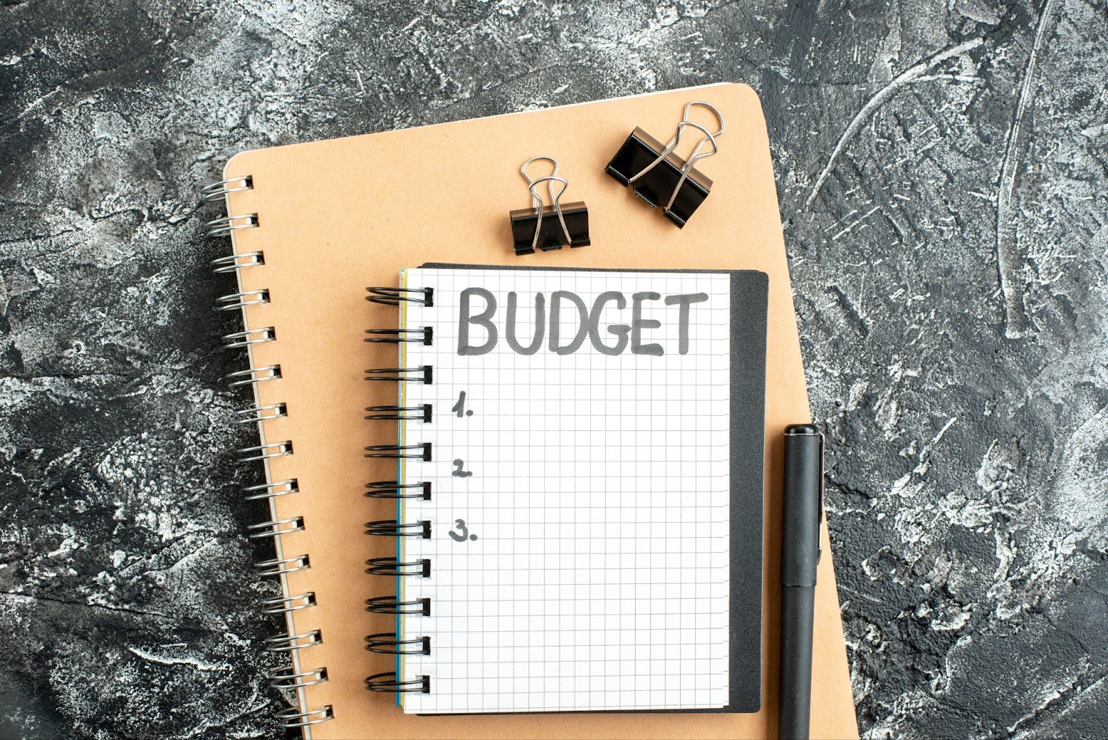  Word “budget” written on a notepad next to a pen and two clips. 