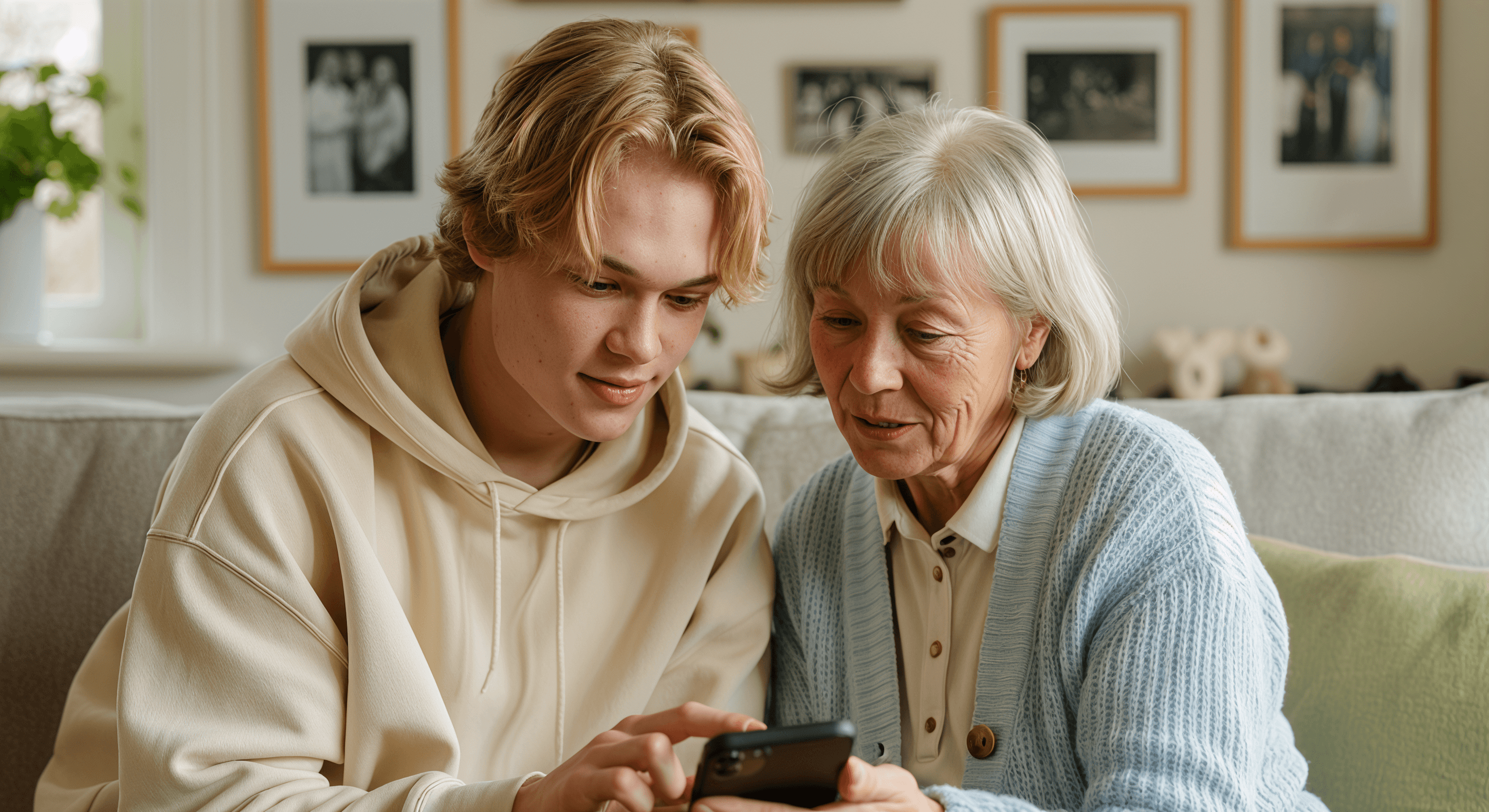 A young man and older woman looking at a smartphone together while sitting on a couch. The man points at the phone.