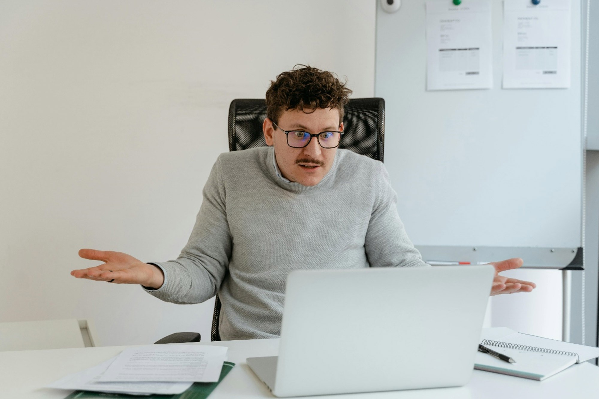 Person sitting at a desk looking confused while working on a laptop