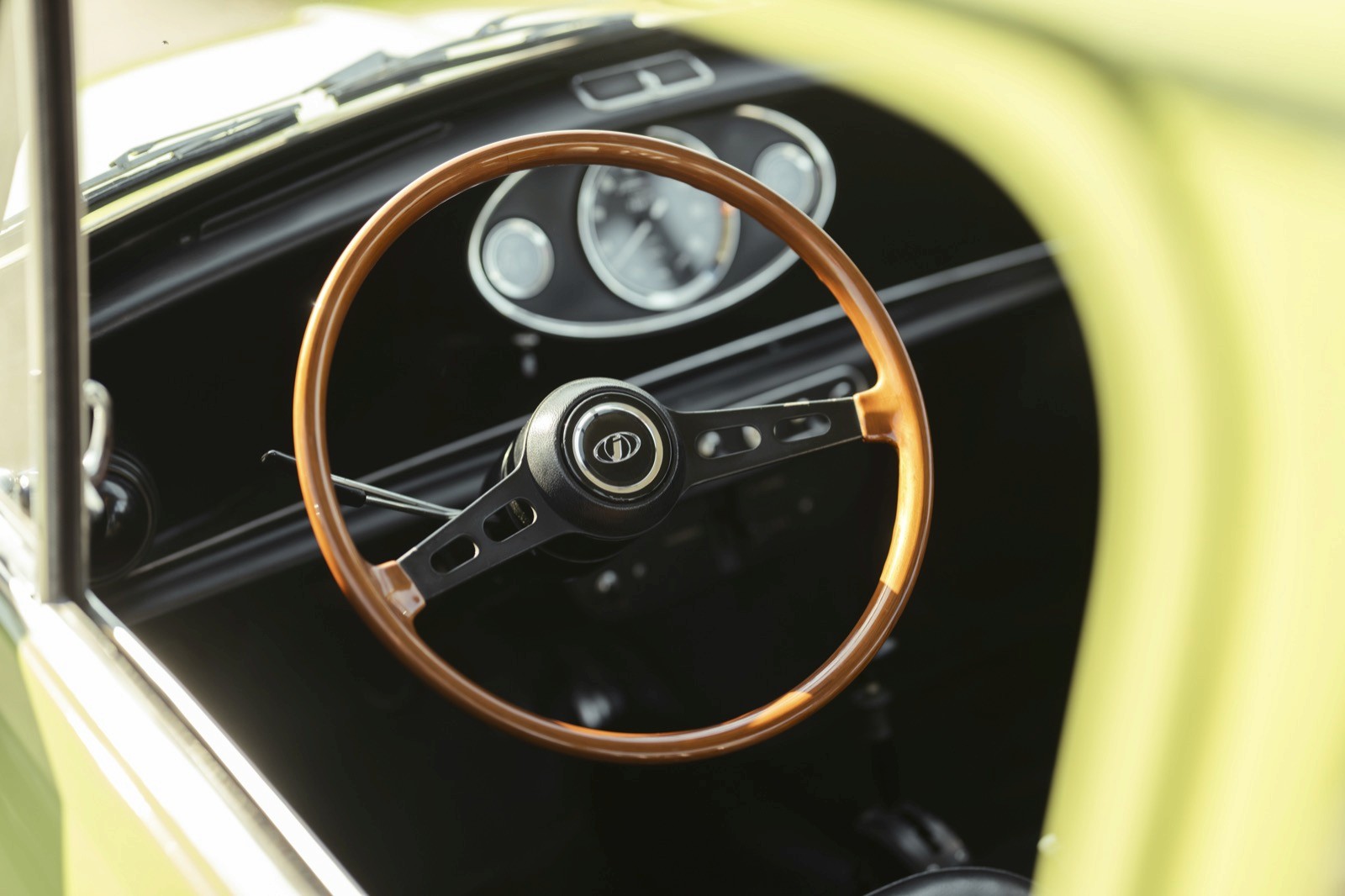 Close-up of a vintage car's interior, featuring a wooden steering wheel and classic dashboard gauges.