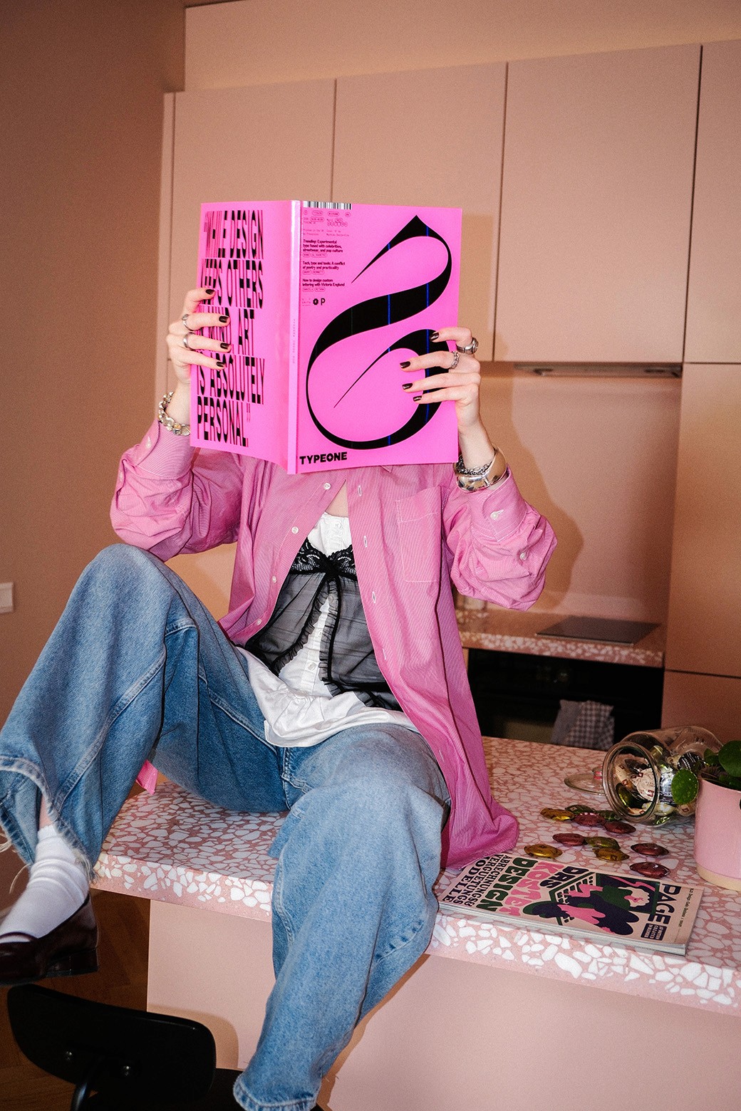 Person sitzt auf Küchenzeile und liest pinkes Magazin