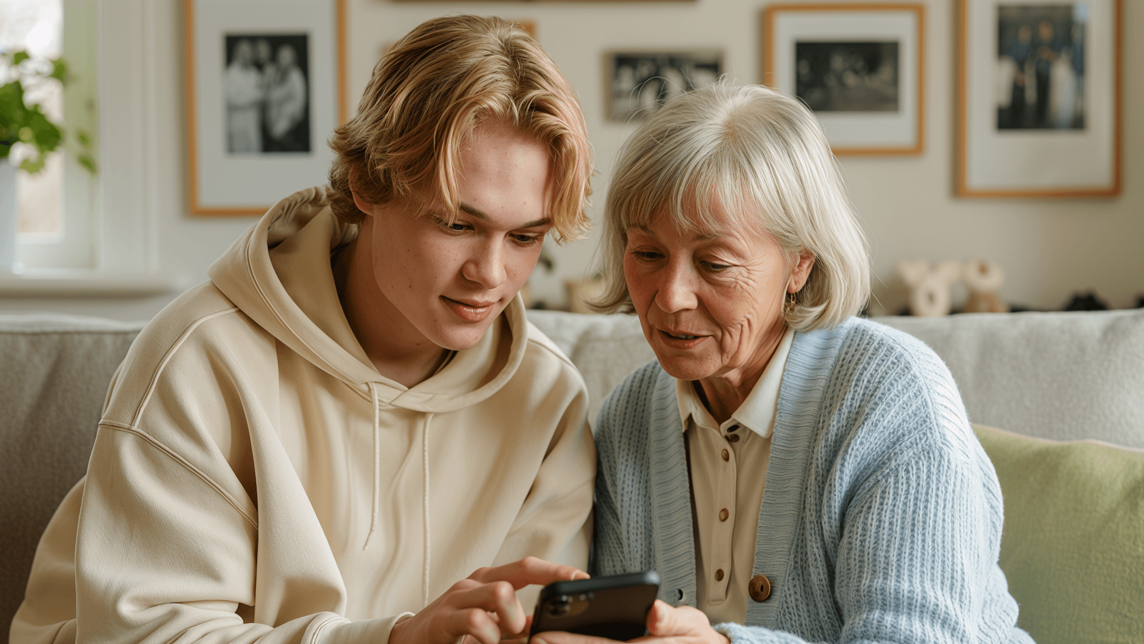A young man and an elderly woman share a moment, looking at a smartphone together in a cozy living room setting.