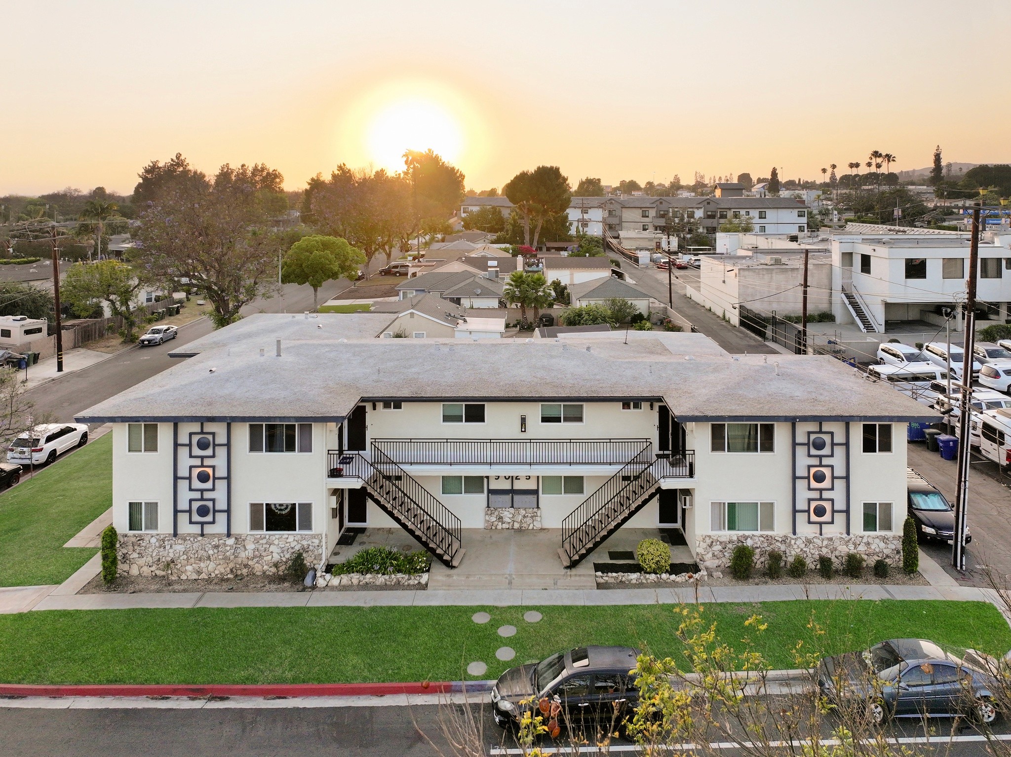 9025 Mills Avenue aerial view showing full apartment building, landscaped lawn and sunset sky.