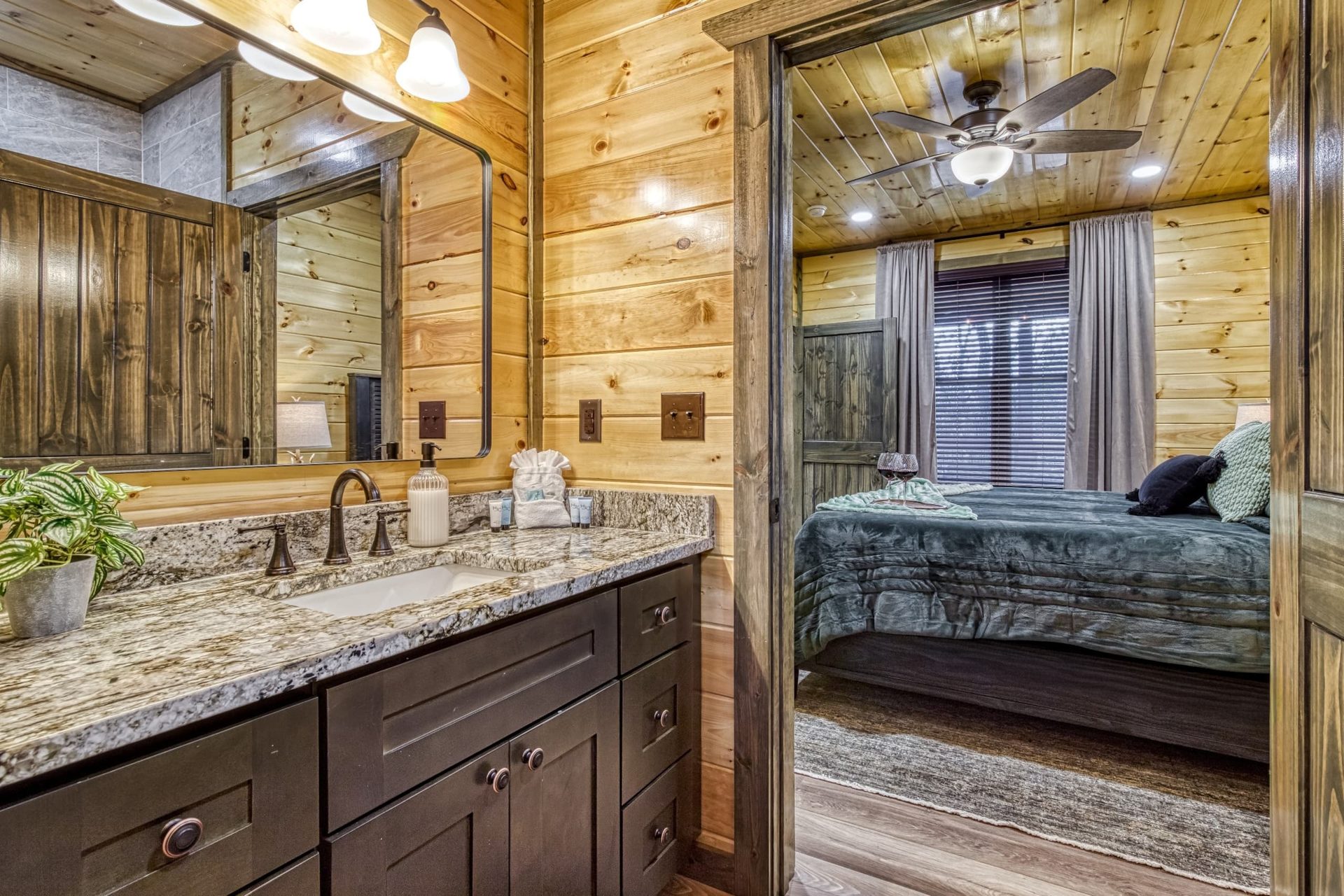 Bathroom vanity with a granite top and framed mirror, the doorway open to the teal-bedding king bedroom