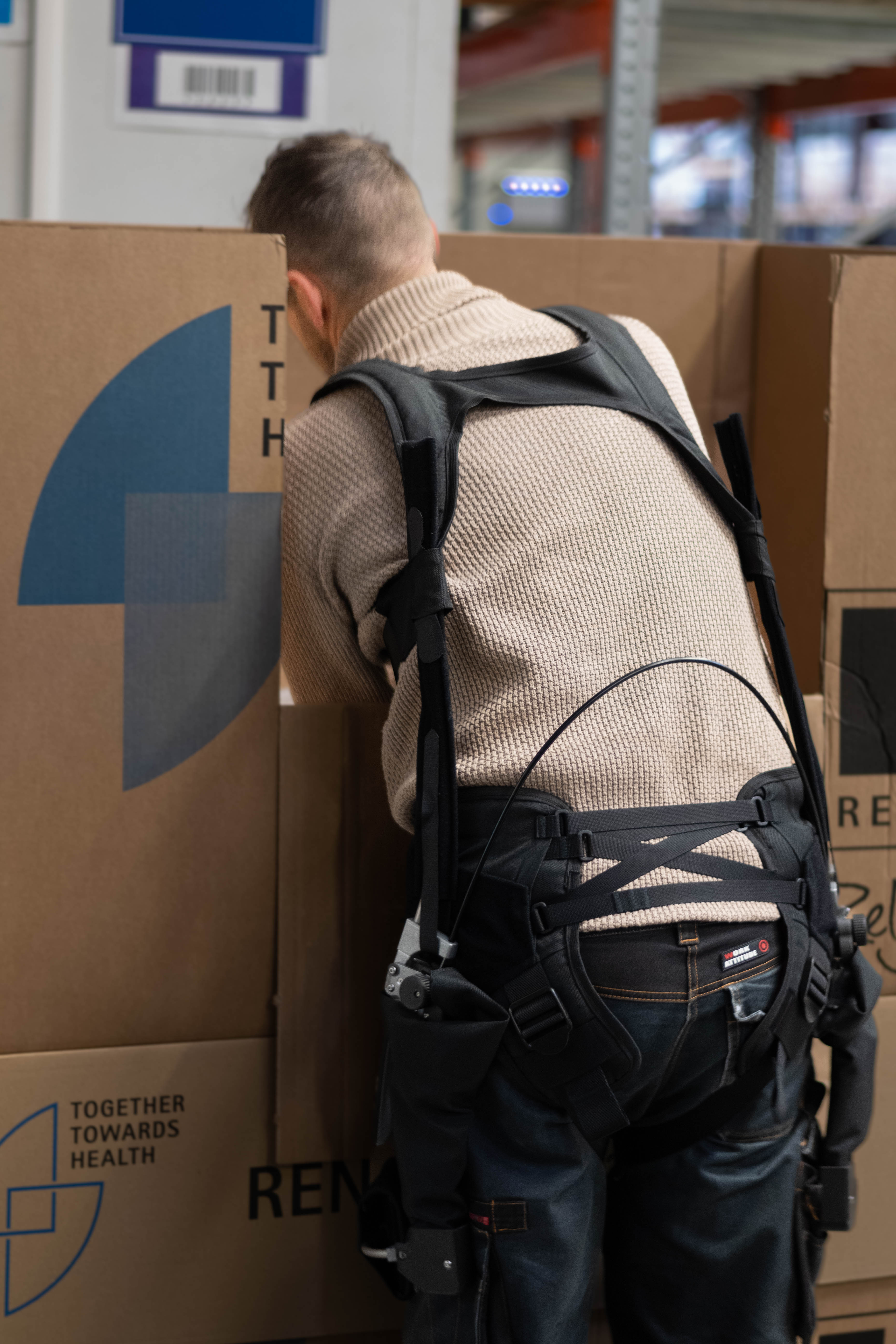 Employé équipé de l’exosquelette Wave soulevant des boîtes en entrepôt, réduisant la charge sur le bas du dos et prévenant les blessures musculosquelettiques.
