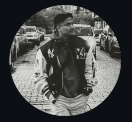 A woman with short curly hair wearing a black t-shirt looks into the camera.