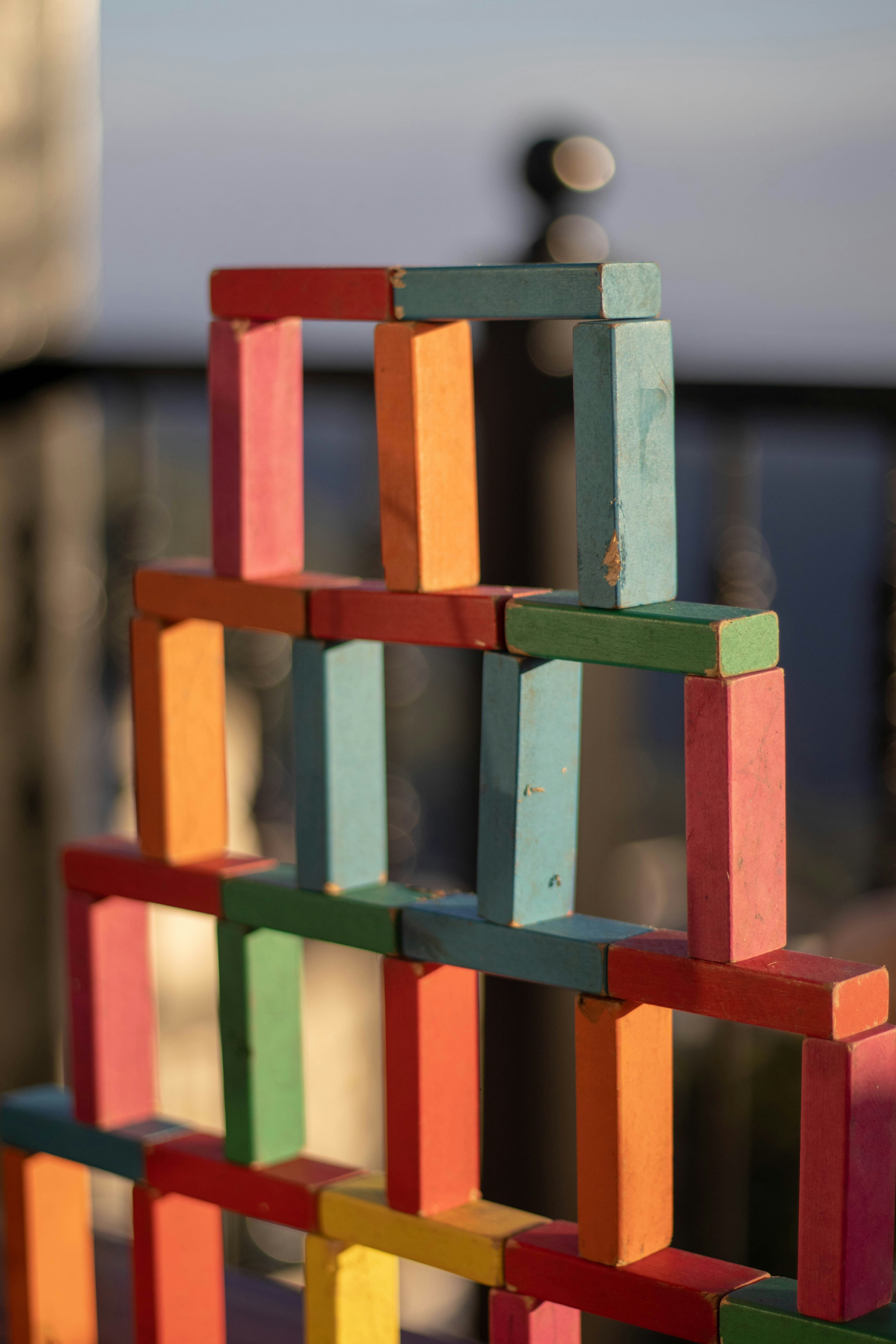 A colorful tower made of books, reaching high against a blurred background, with a small figure on top.