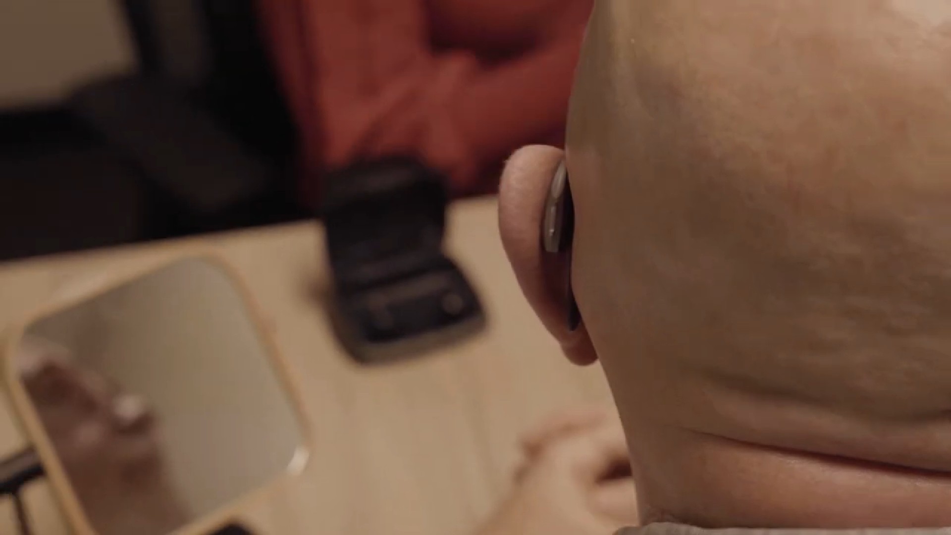 A close-up of a person’s hand holding a black mobile phone next to an open book on a table.