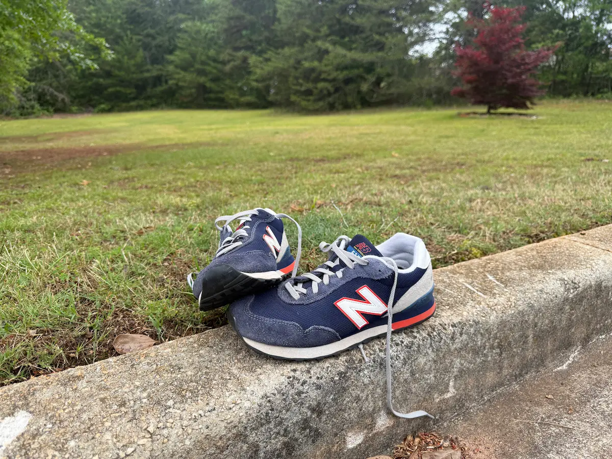 A pair of blue sneakers resting on a curb beside a grassy field and trees on a quiet spring day.