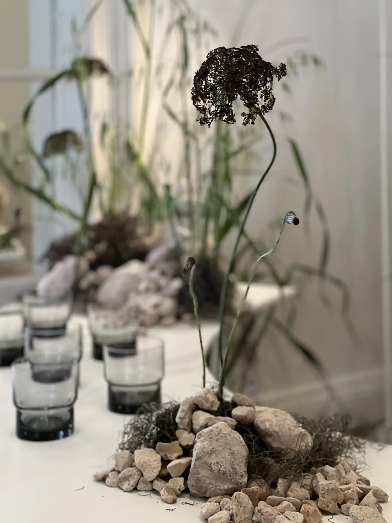 Mesa decorada con piedras, flores secas y vasos de vidrio para ambientación natural con enfoque botánico.