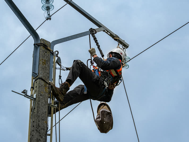 Monteur en harnais sur un poteau de ligne électrique