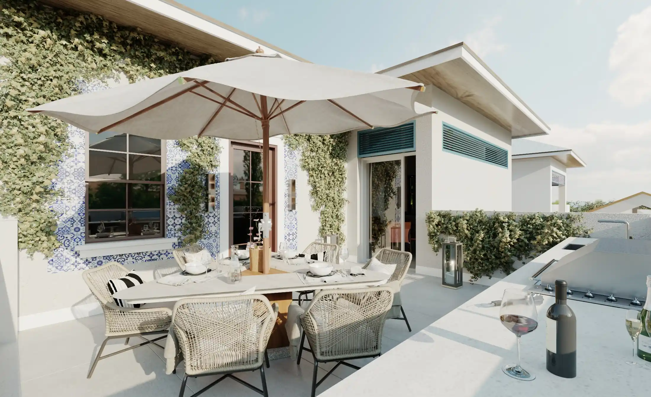 Outdoor patio dining area with a large white umbrella shading a table and wicker chairs, surrounded by ivy-covered walls and potted greenery, with a wine bottle and glasses on a nearby counter.