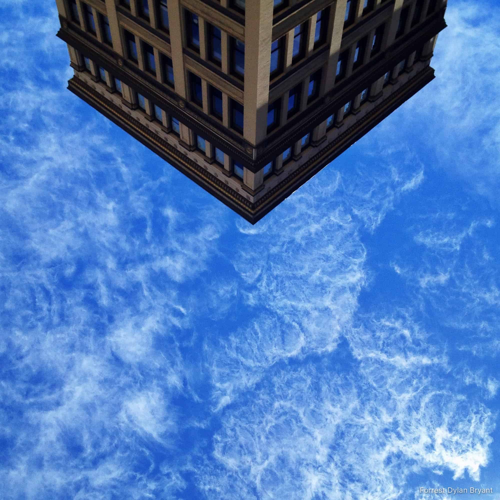 Inverted image with an old office building at the top and intricate clouds in a bright blue sky below.