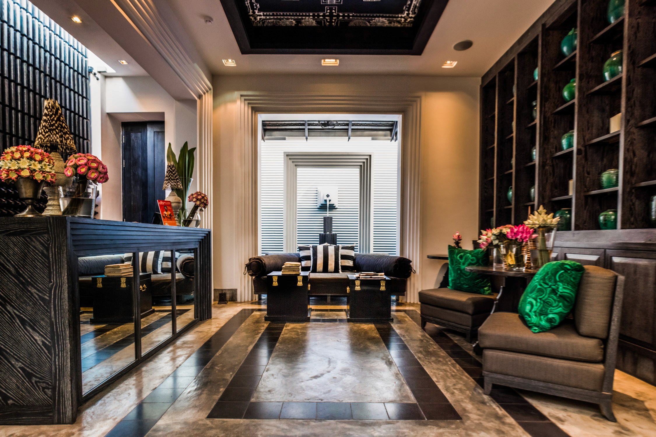 A modern hotel lobby with a reception desk, plush seating area, and floral arrangements under warm interior lighting.