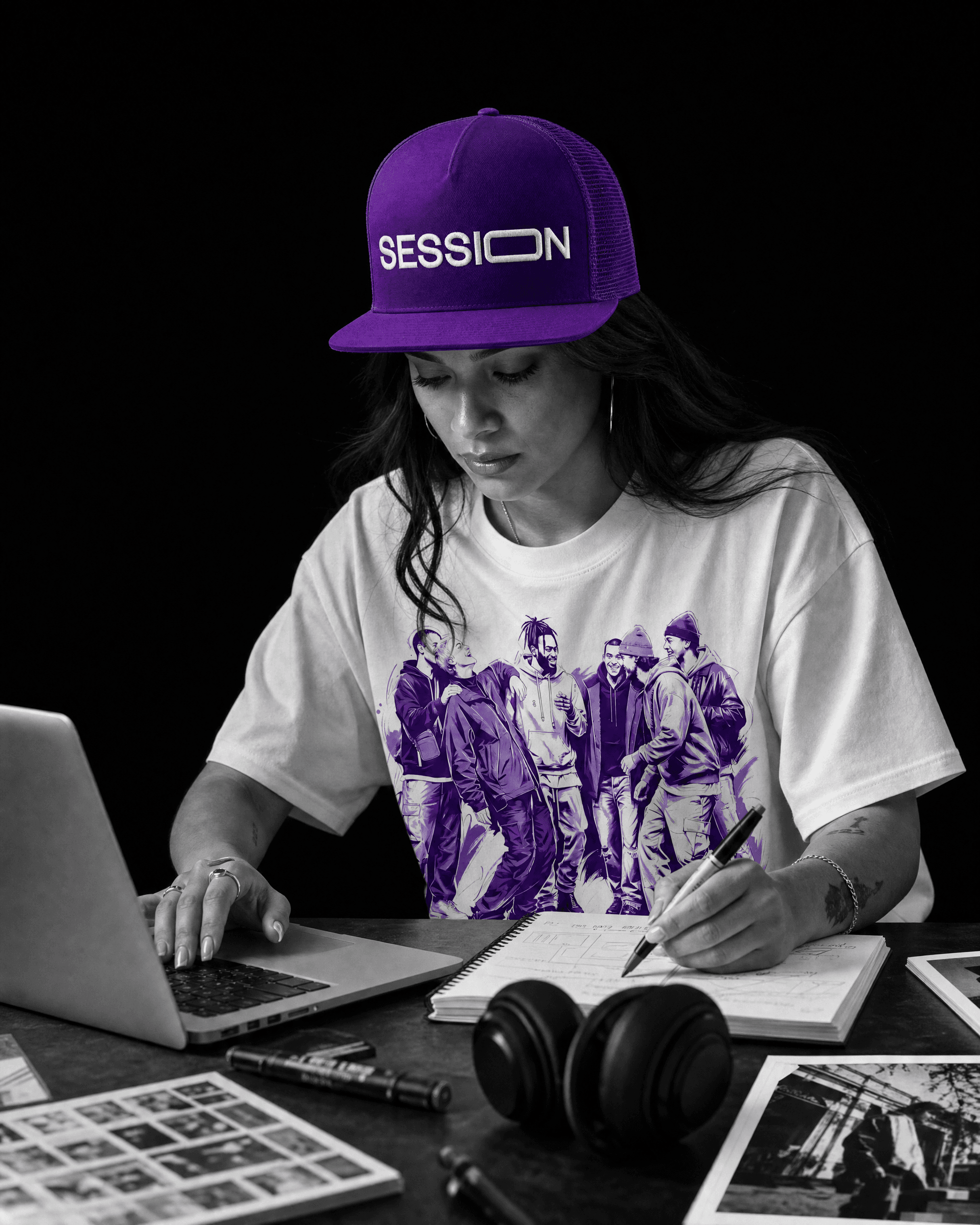 Woman wearing a purple Session Zone cap and white community-graphic T-shirt while using a laptop and notebook.