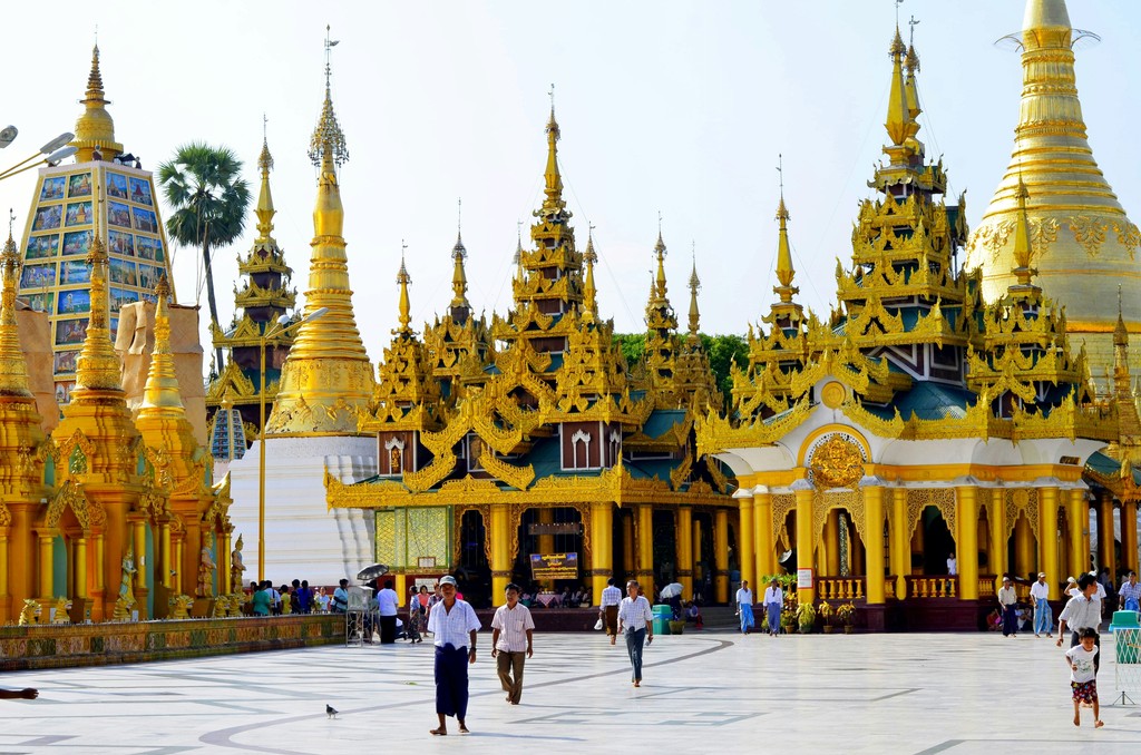 The Shwedagon Pagoda in Yangon, Myanmar, stands majestically with its golden spires and intricate architecture, attracting numerous visitors who explore the historic and sacred Buddhist site.