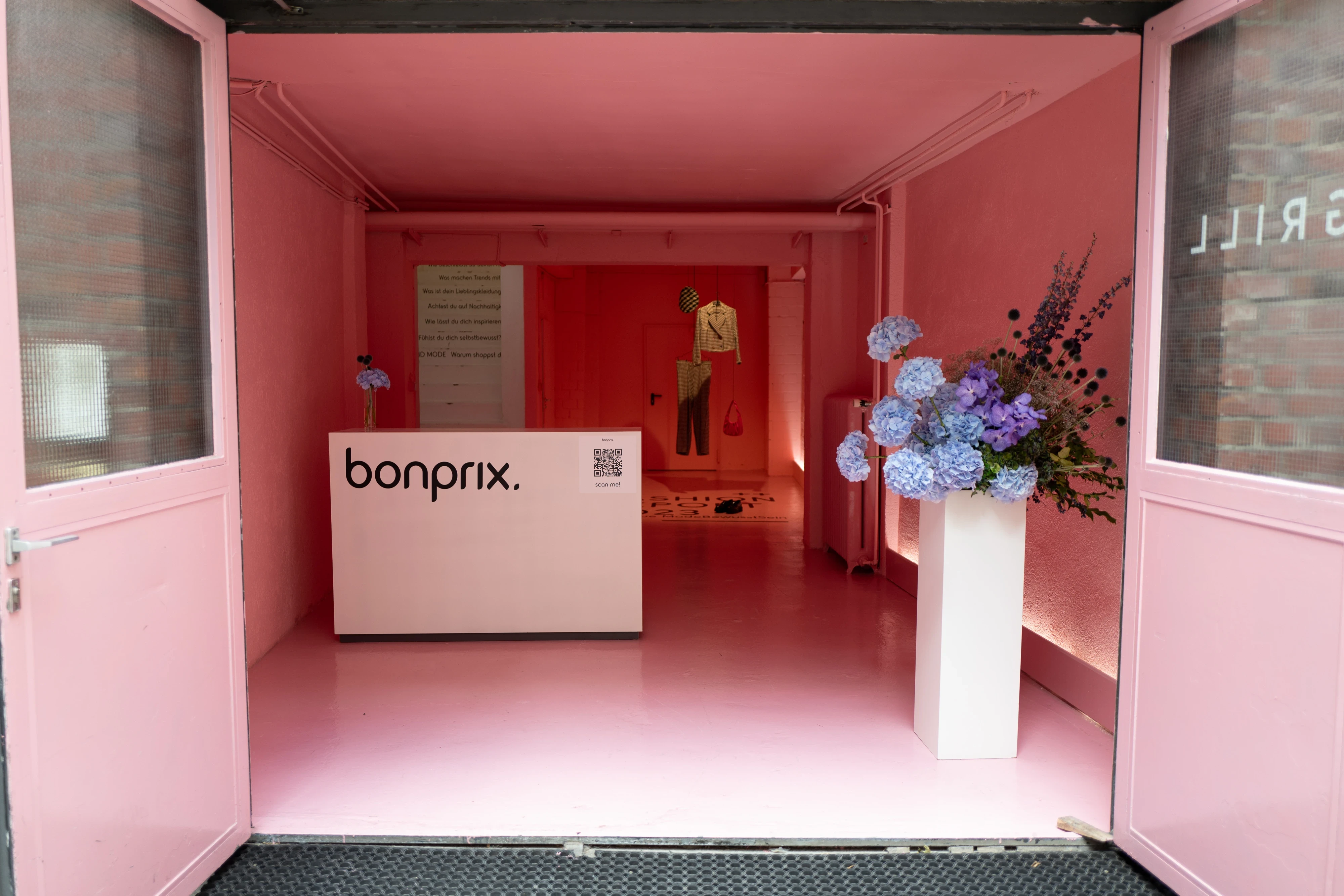 Pink entrance of the Bonprix pop-up with white counter, QR code panel and hydrangea bouquet.