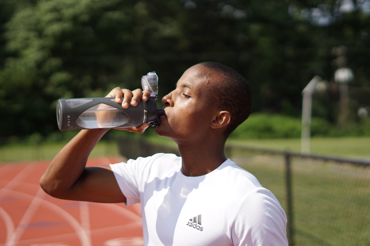 An athlete pausing to drink from a sports bottle, replacing the water and electrolytes lost through sweat.