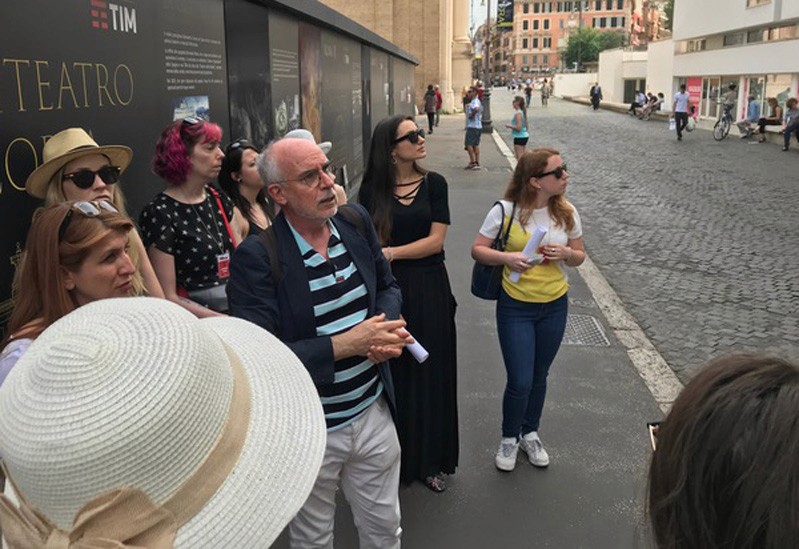 A man giving a tour and a lecture to some students while standing in the street.