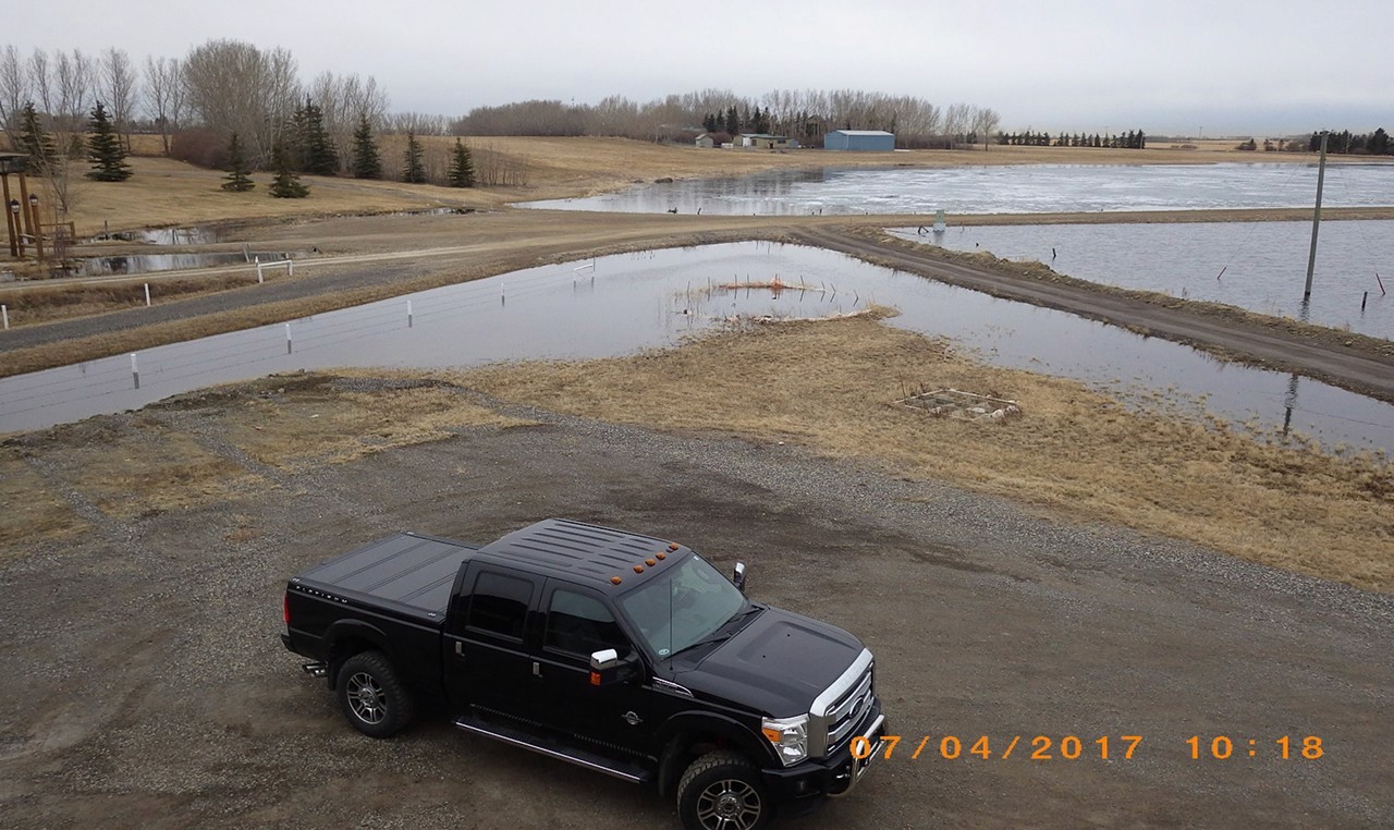 Flooded residential property and access roads with survey markers near stormwater pond