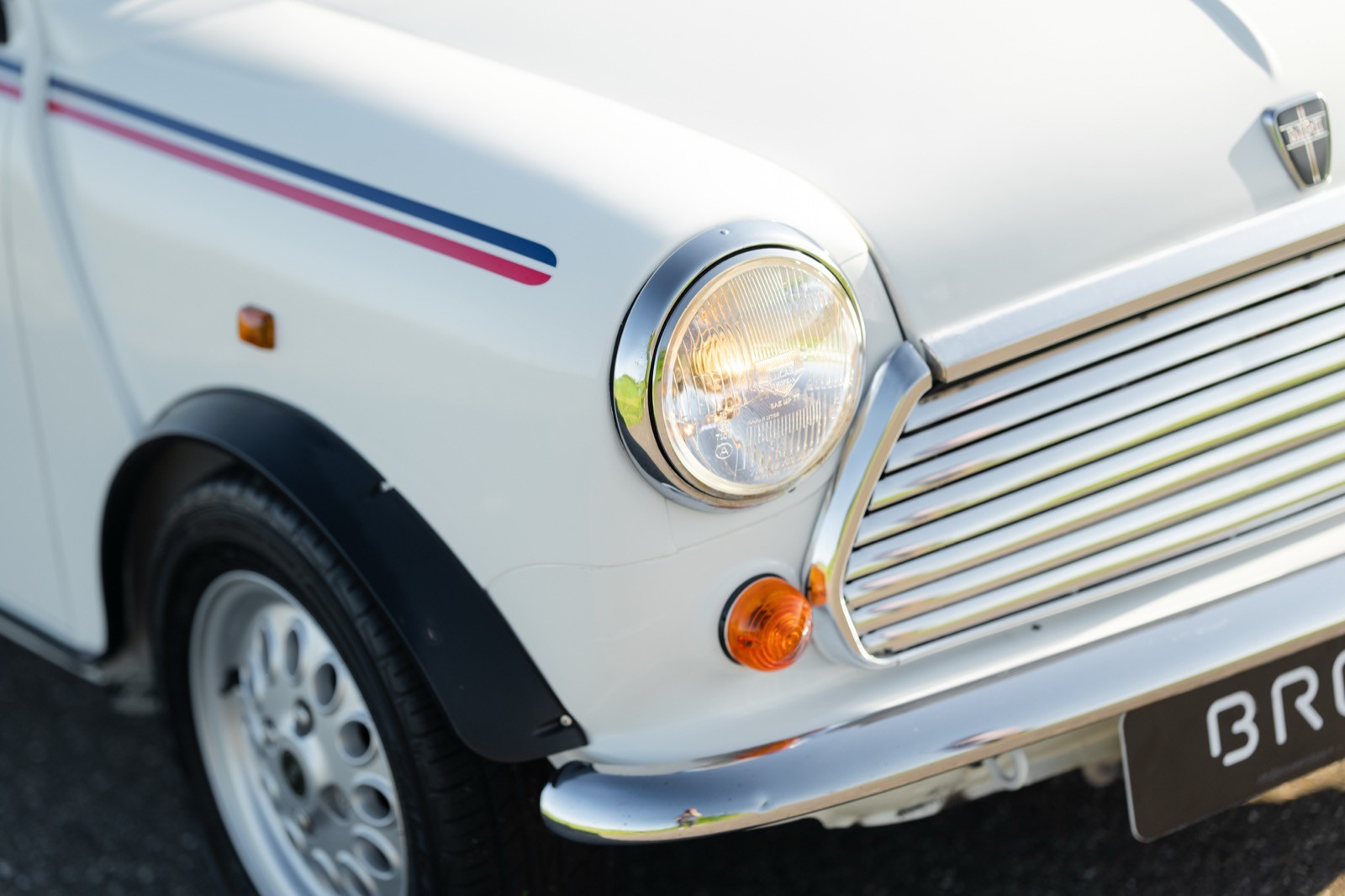 Close-up of the front corner of a white vintage car, featuring its round headlight and chrome details.