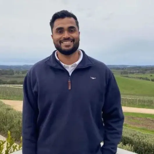 Man in navy pullover, smiling outdoors.