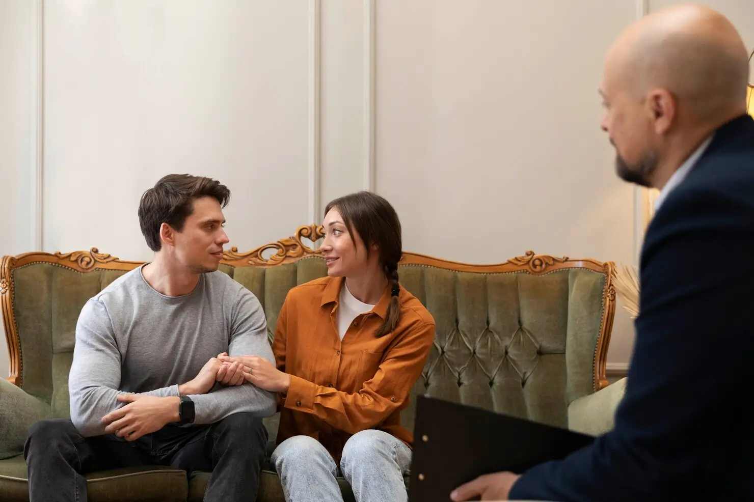 Relationship counseling session with a couple holding hands on a green vintage sofa.