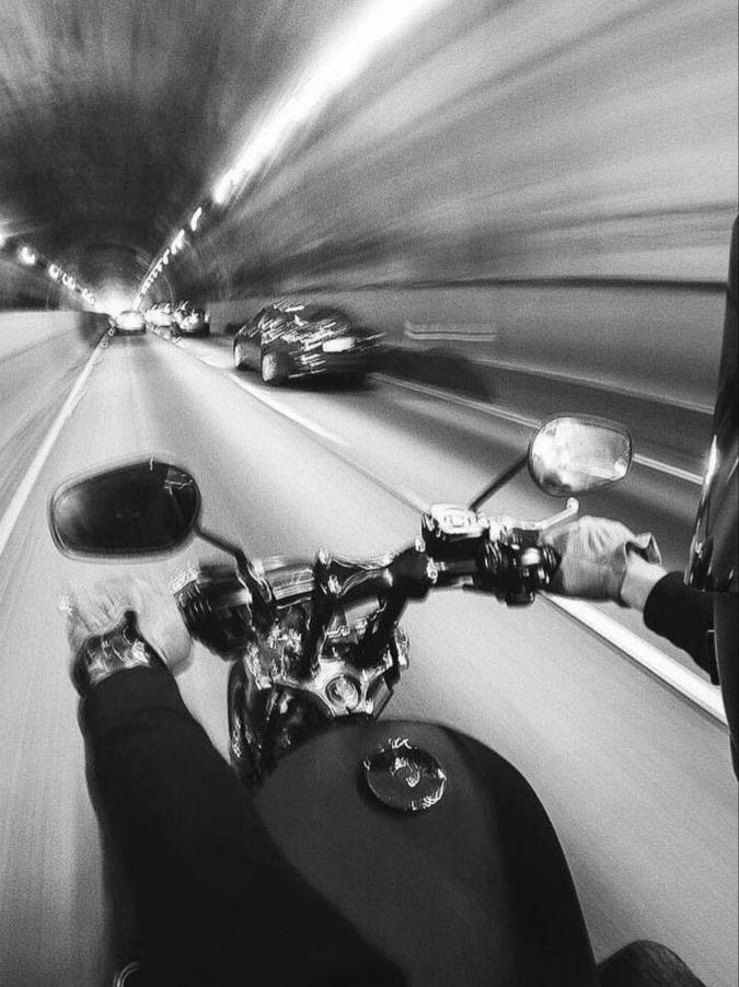 This may contain: a man riding a motorcycle down a street next to a traffic filled tunnel at night