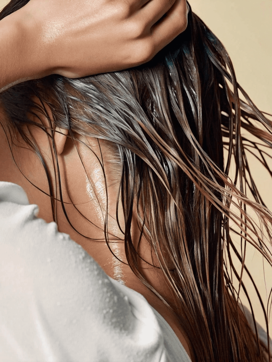 A woman with a radiant complexion lying down with a golden facial mask applied to her skin. She is wrapped in a warm orange towel, with sunlight casting a soft glow on her face, creating a relaxing and rejuvenating spa atmosphere.