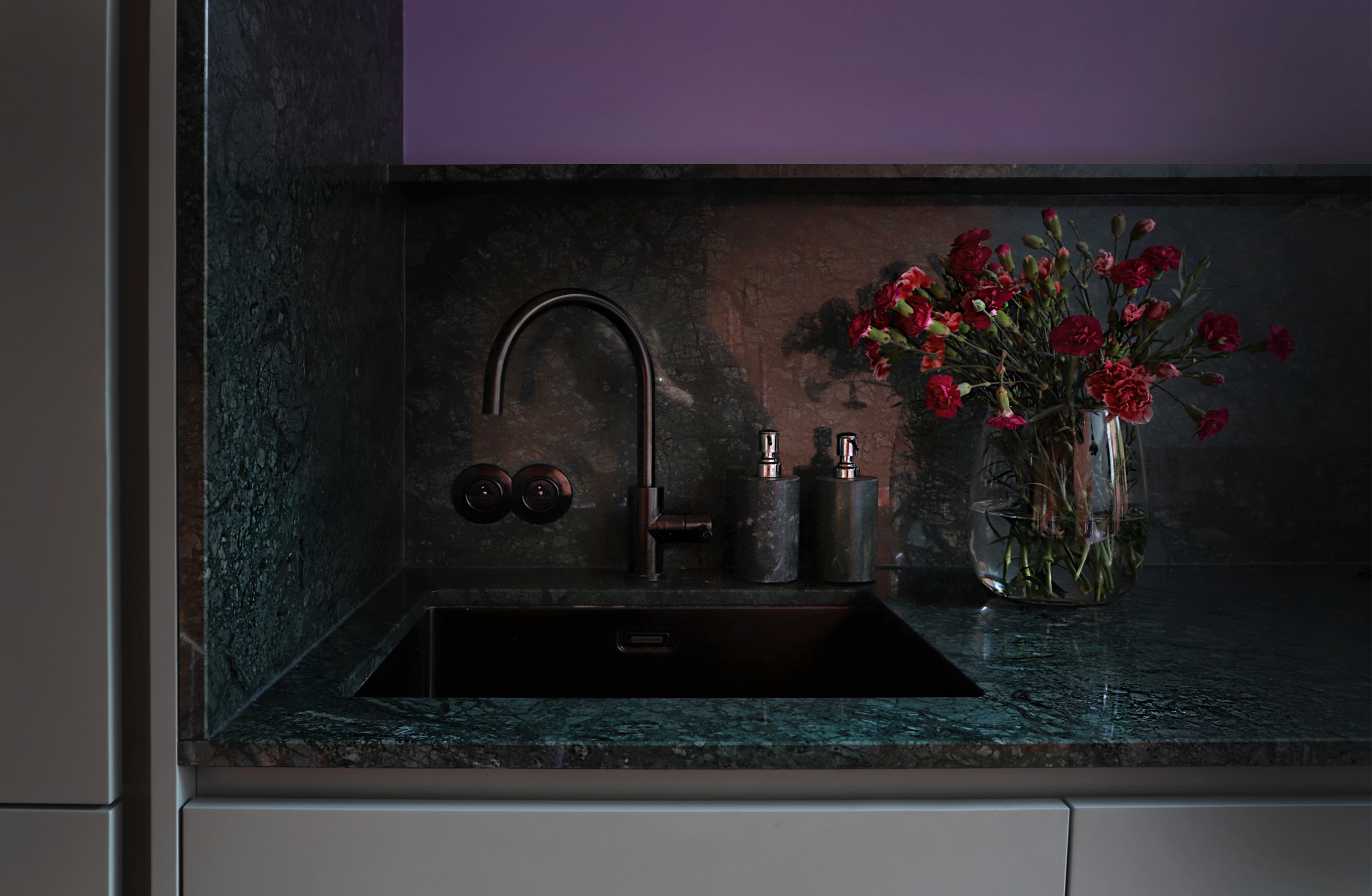 Green marble kitchen niche with dark faucet and floral arrangement — minimalist interior design by ODA Architecture Belgium