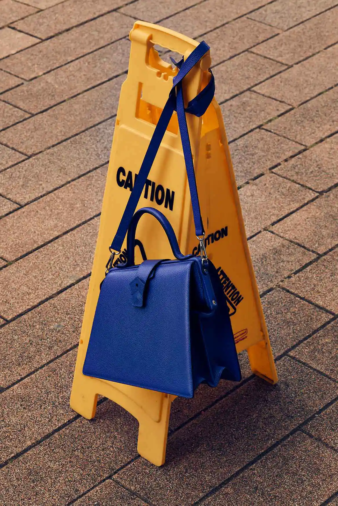 A blue bag hangs from a yellow tripod stand on cobblestone ground.