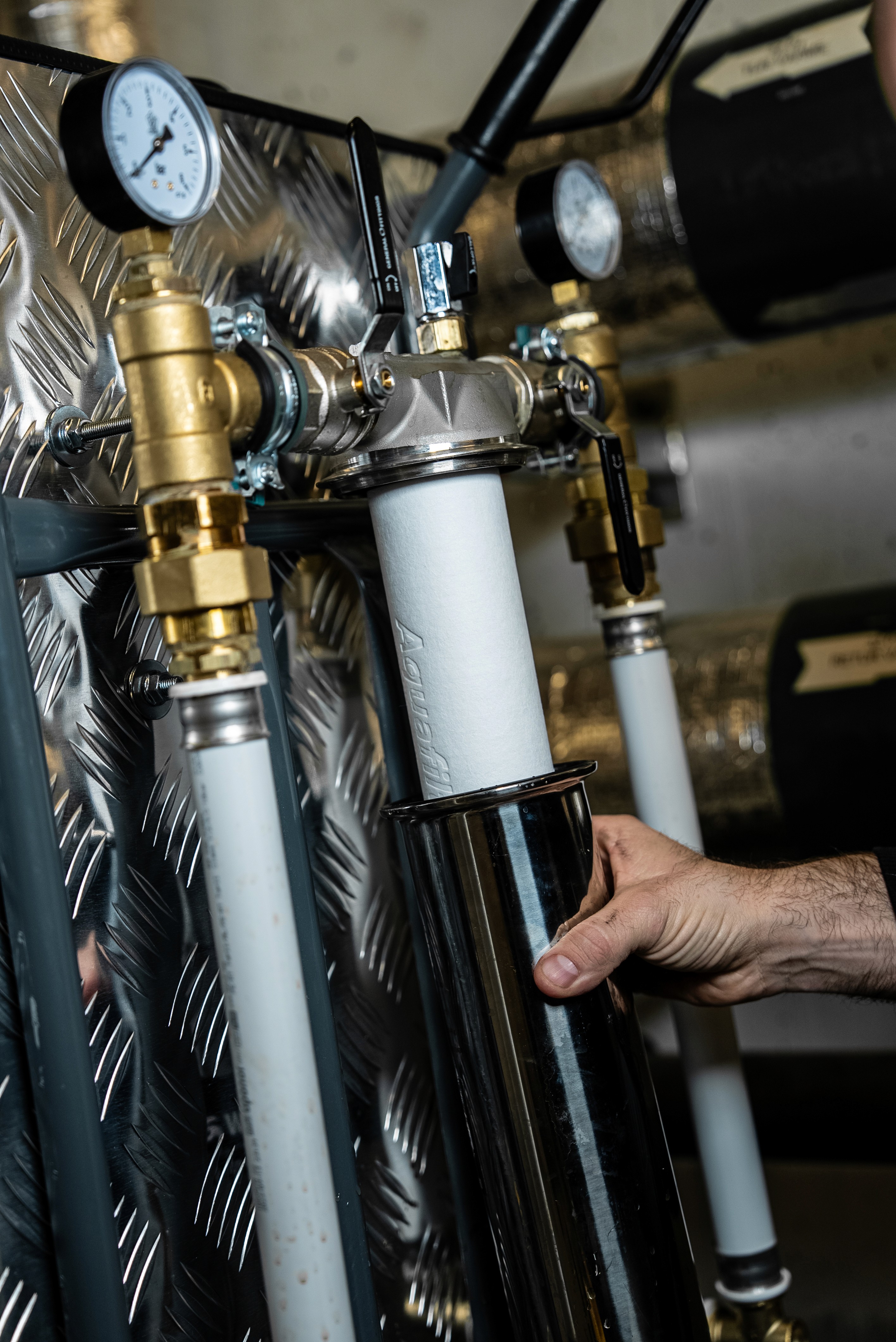Man wearing a plaid shirt and cap working on a laptop and holding a coffee cup in a cafe.