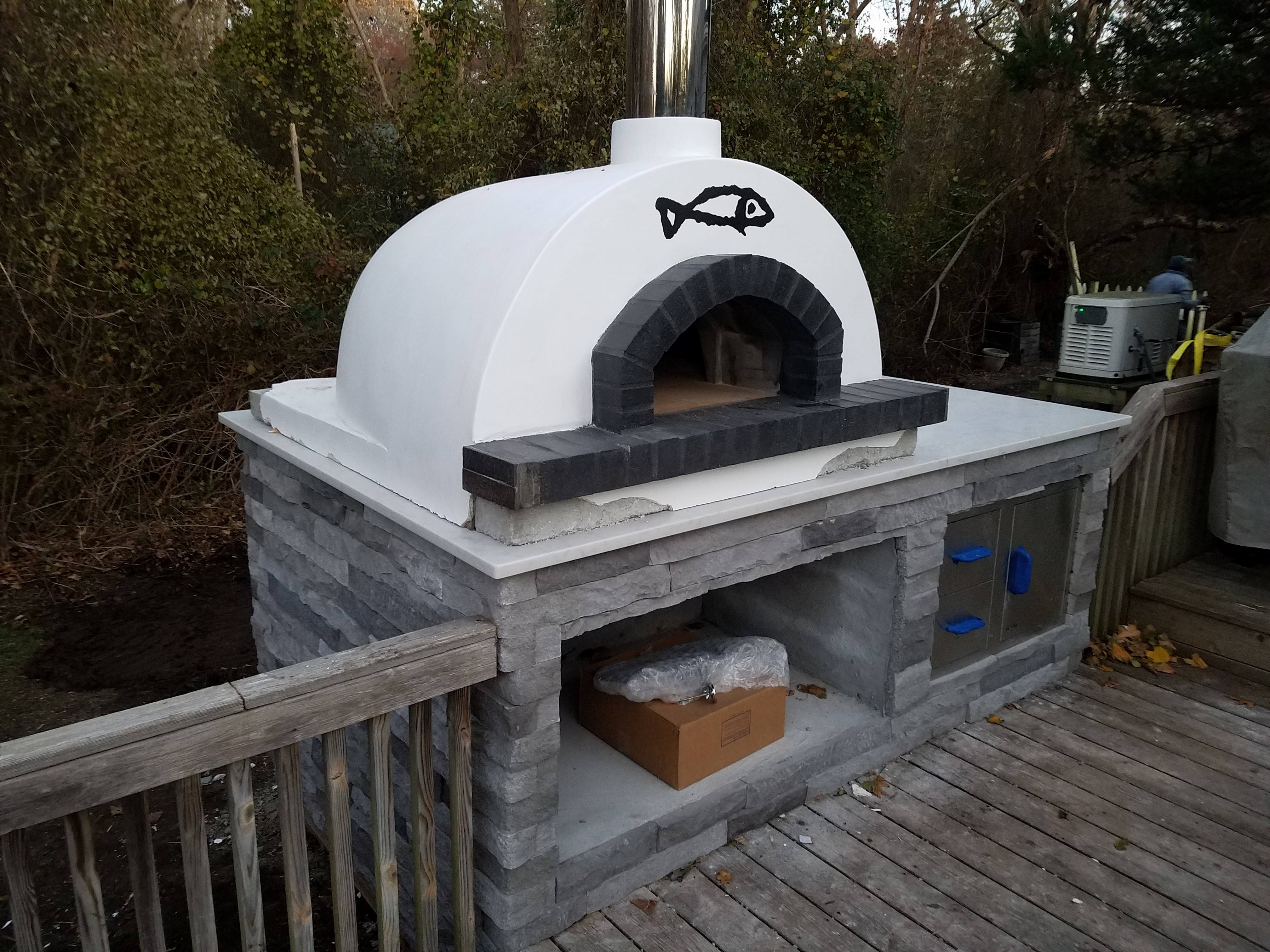 White dome pizza oven on stone base with fish accent and wood storage