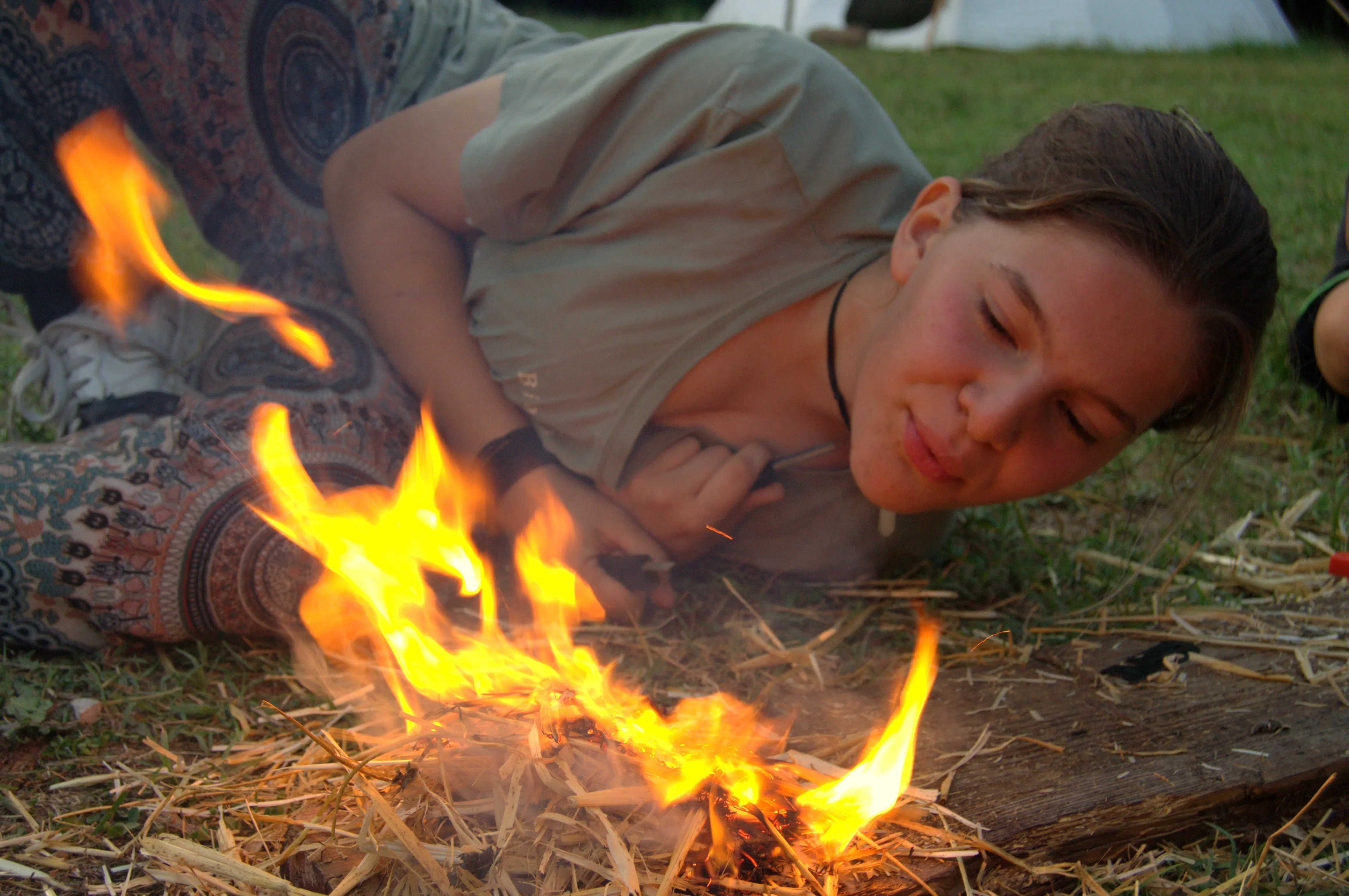 Ragazza accende fuoco durante attività di sopravvivenza in campo avventura estivo per ragazzi, summer camp esperienziale e corso di crescita personale