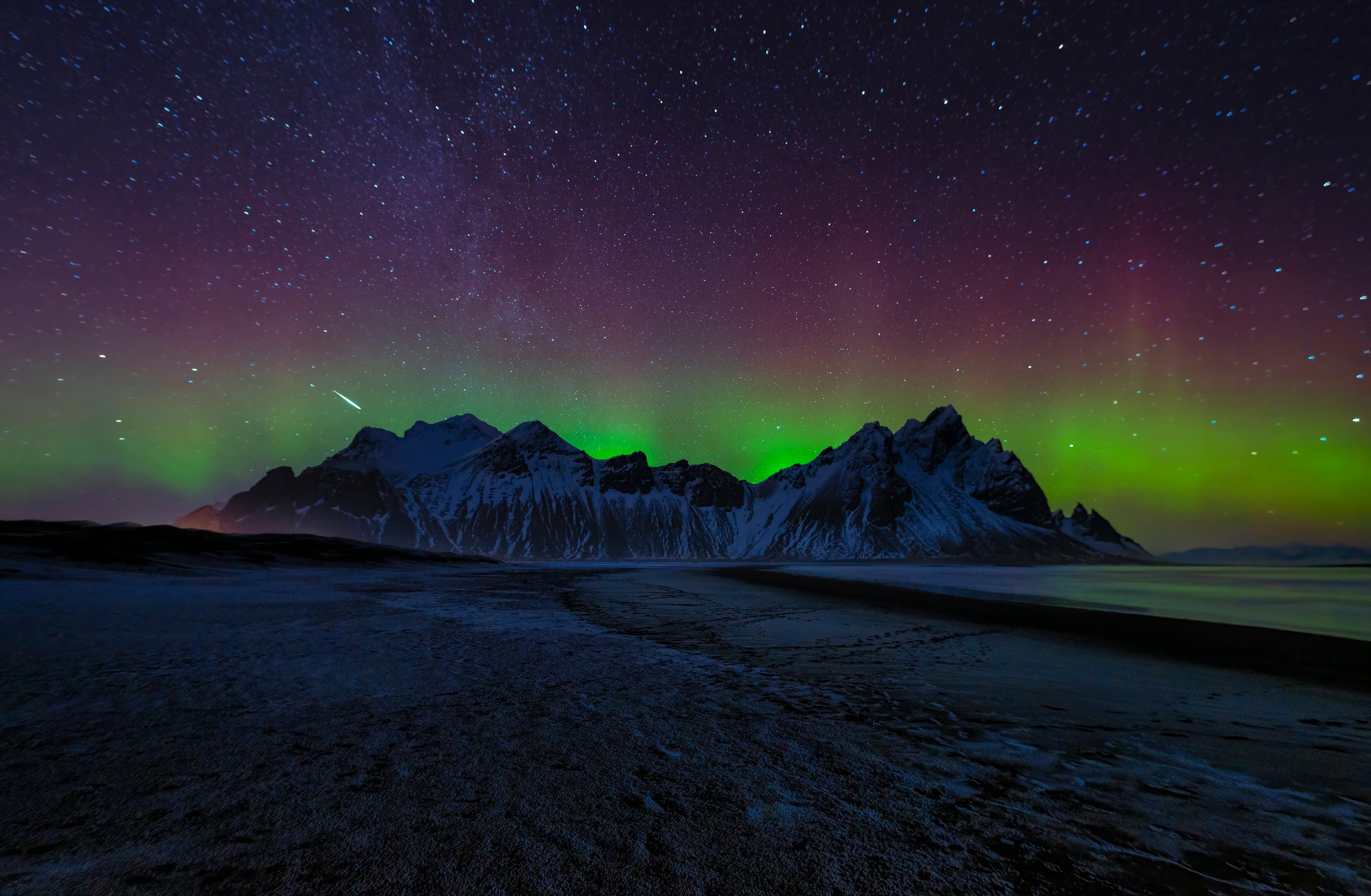 Aurora borealis over snow-capped mountains and starry sky