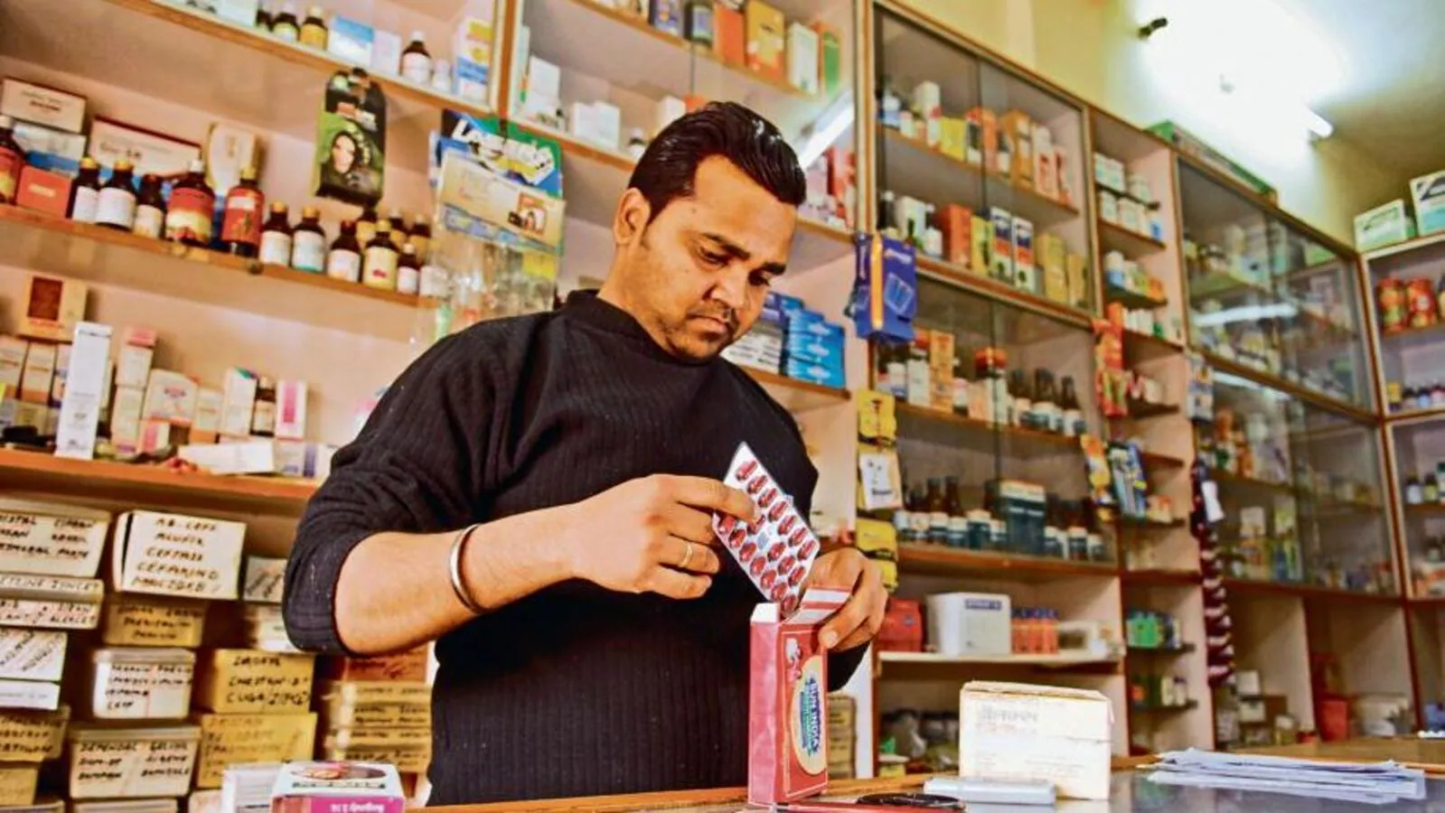 Indian pharmacist organizing medicine strips in a retail pharmacy shop