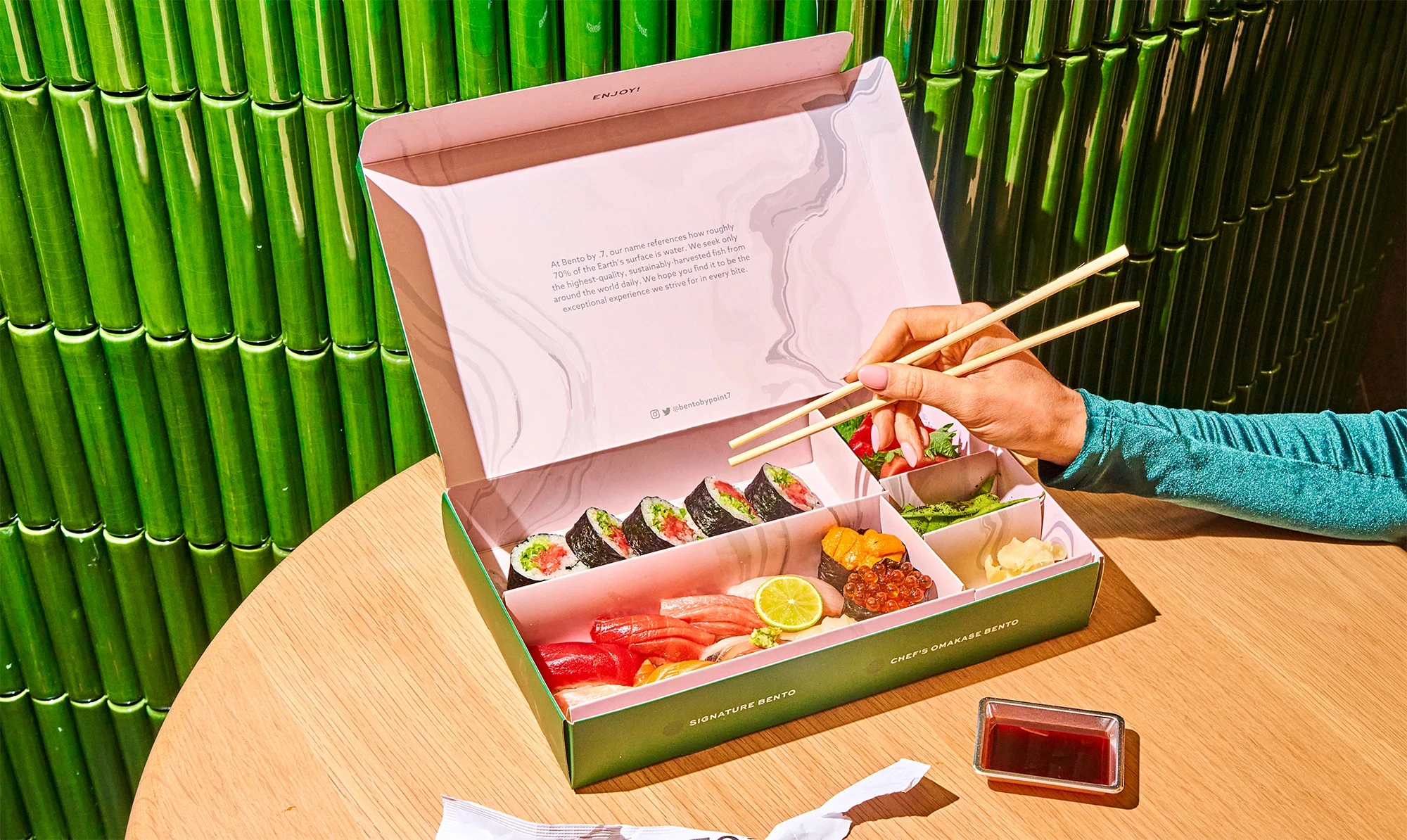 Sushi bento box and chopsticks against green tiles