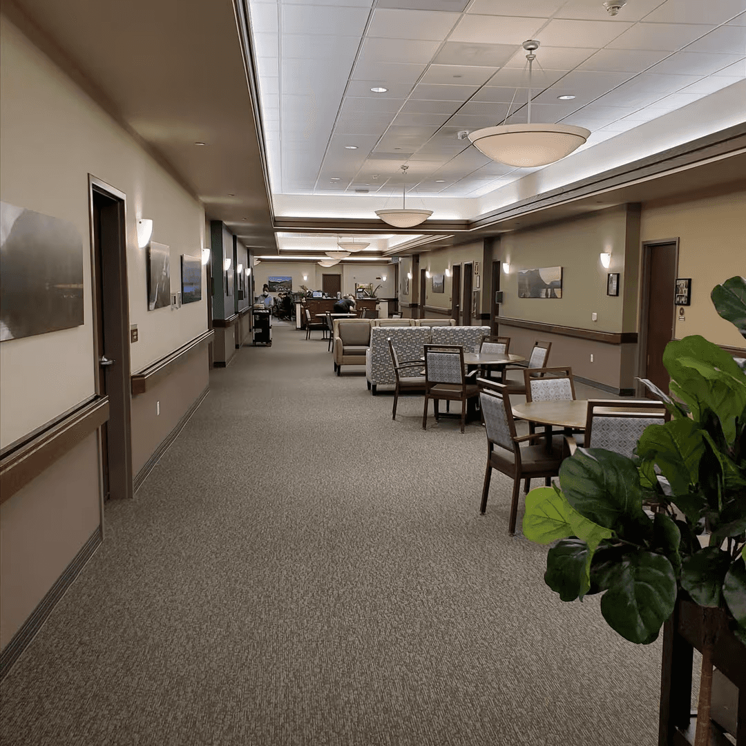 Wide memory care corridor with tables and seating areas where residents can gather and rest.