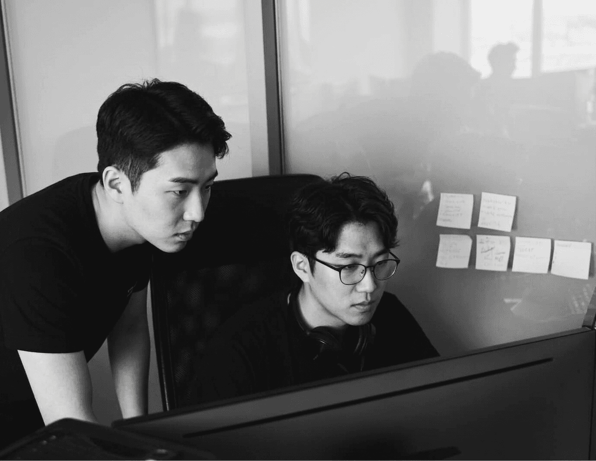 Black and white photo of two people looking at a computer screen with papers on wall
