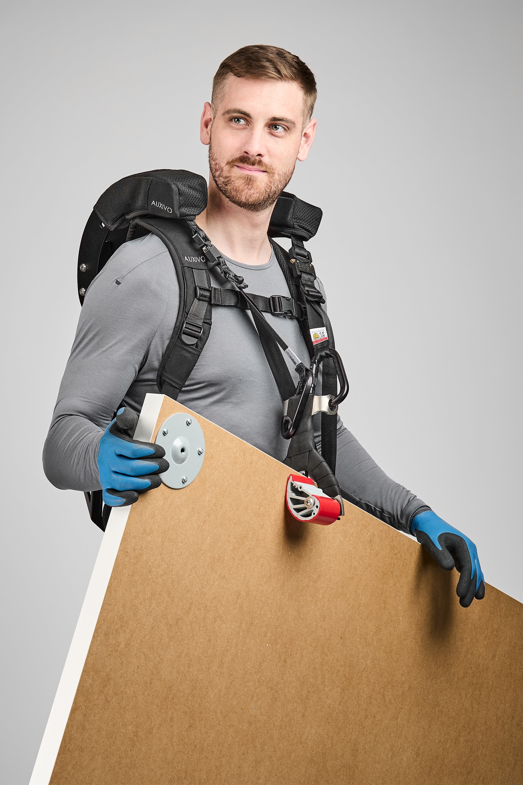 Man wearing a CarrySuit exoskeleton carrying a wooden panel, designed to reduce back pain and improve efficiency in physical work and handling.