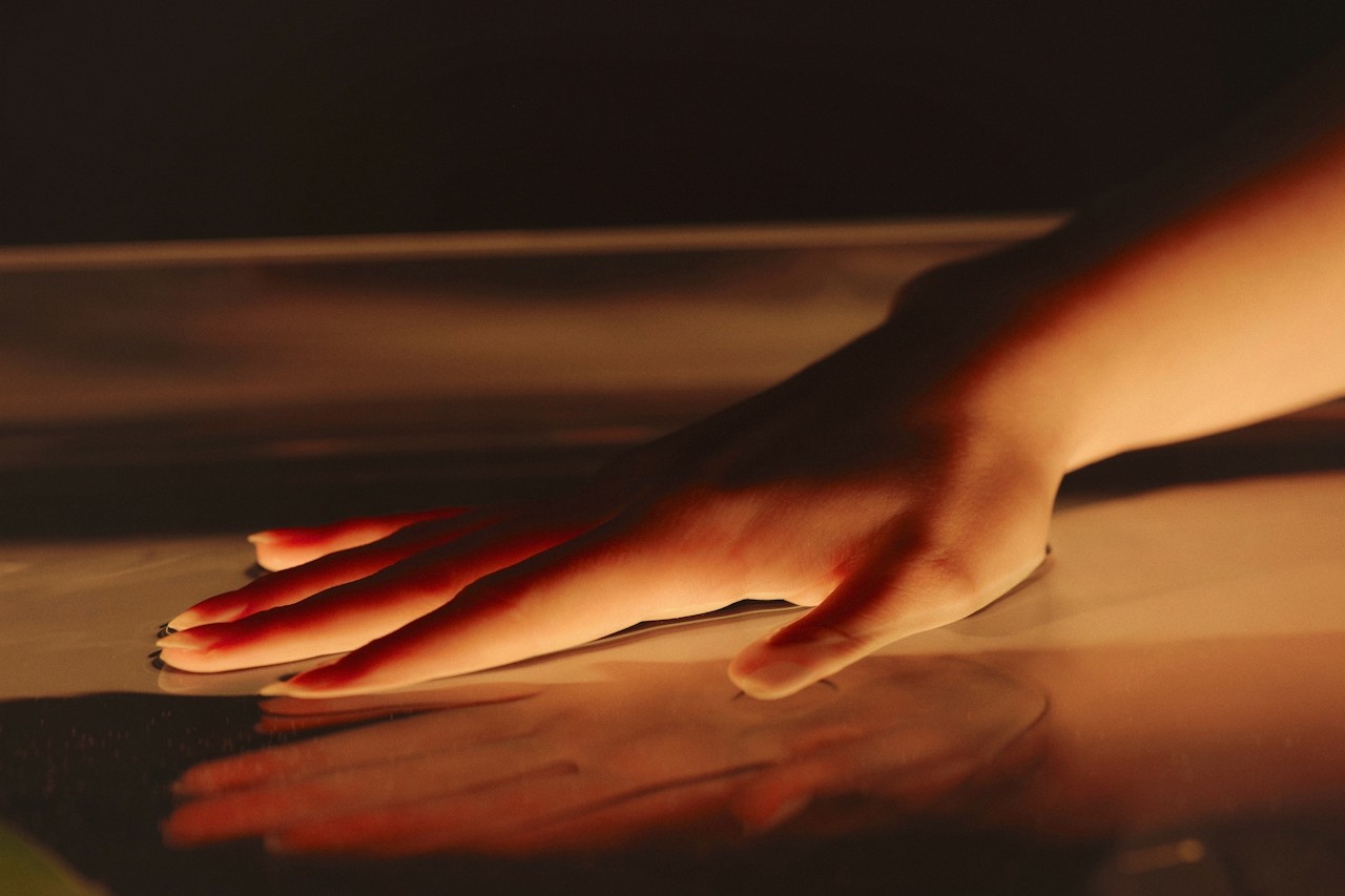 A softly lit hand touching a reflective surface.