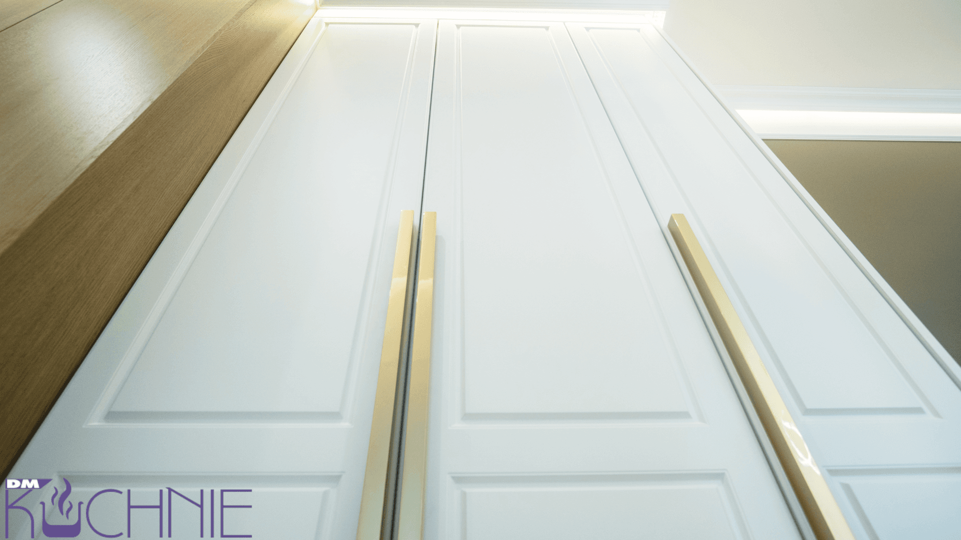 Szafa z białymi frontami meblowymi ze złotymi uchwytami w zabudowie wykonanej na wymiar w Warszawie