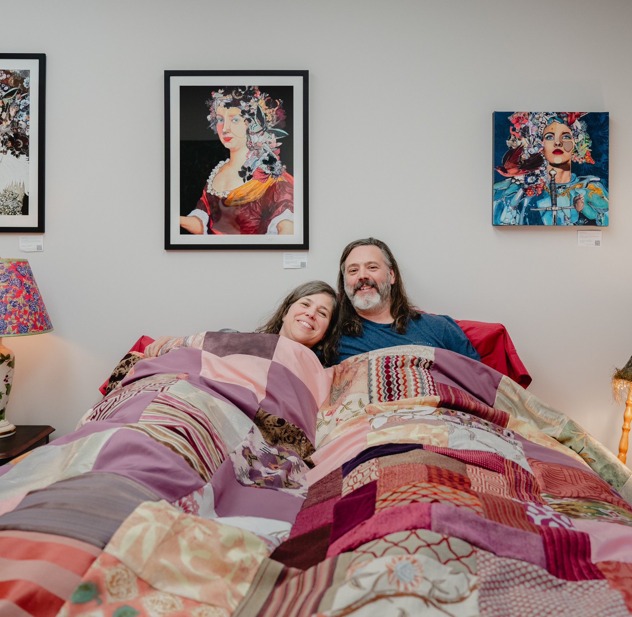 Couple allongé sous une courtepointe colorée dans une chambre du gîte R112-Nord, décorée de tableaux artistiques aux couleurs vives.